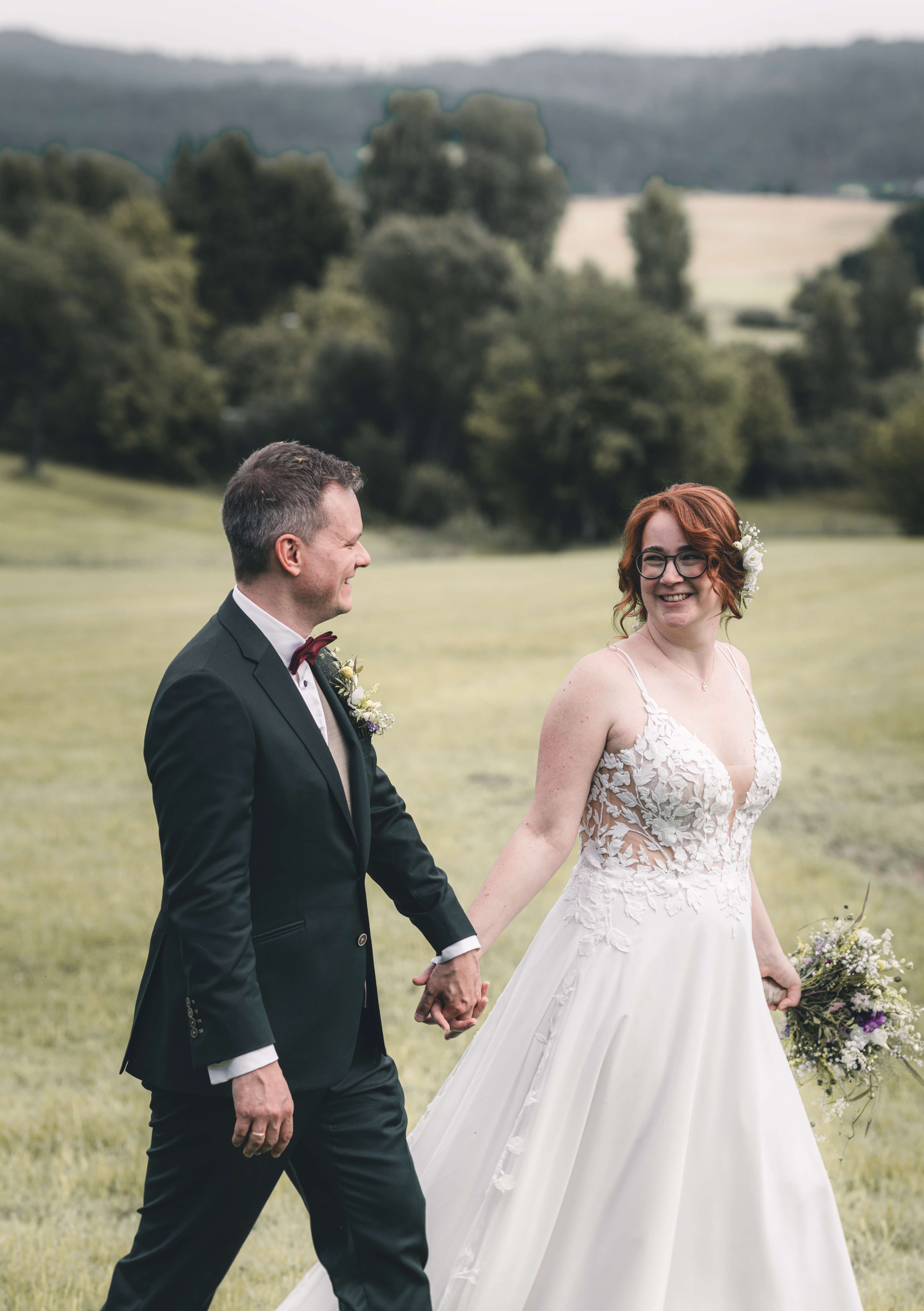 Brautpaar läuft Hand in Hand über eine Wiese während einer Ganztages-Hochzeitsreportage nach standesamtlicher Trauung in Pirna und Feier in der Alten Schäferei Oppach