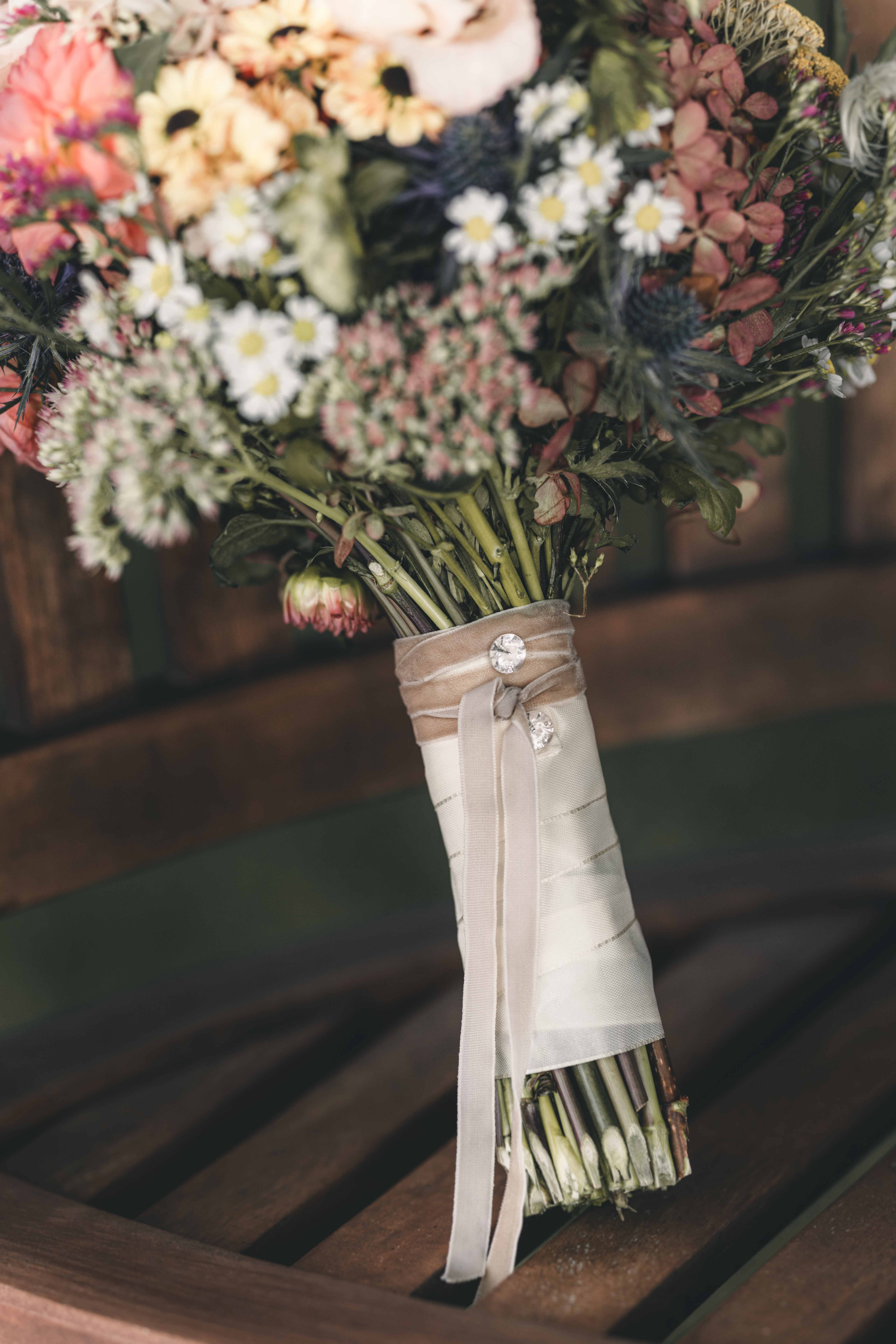 Nahaufnahme des mit Samtband und Glitzersteinen gewickelten Stiels des bunten Wiesenblumen-Brautstraußes im Raum Dresden.