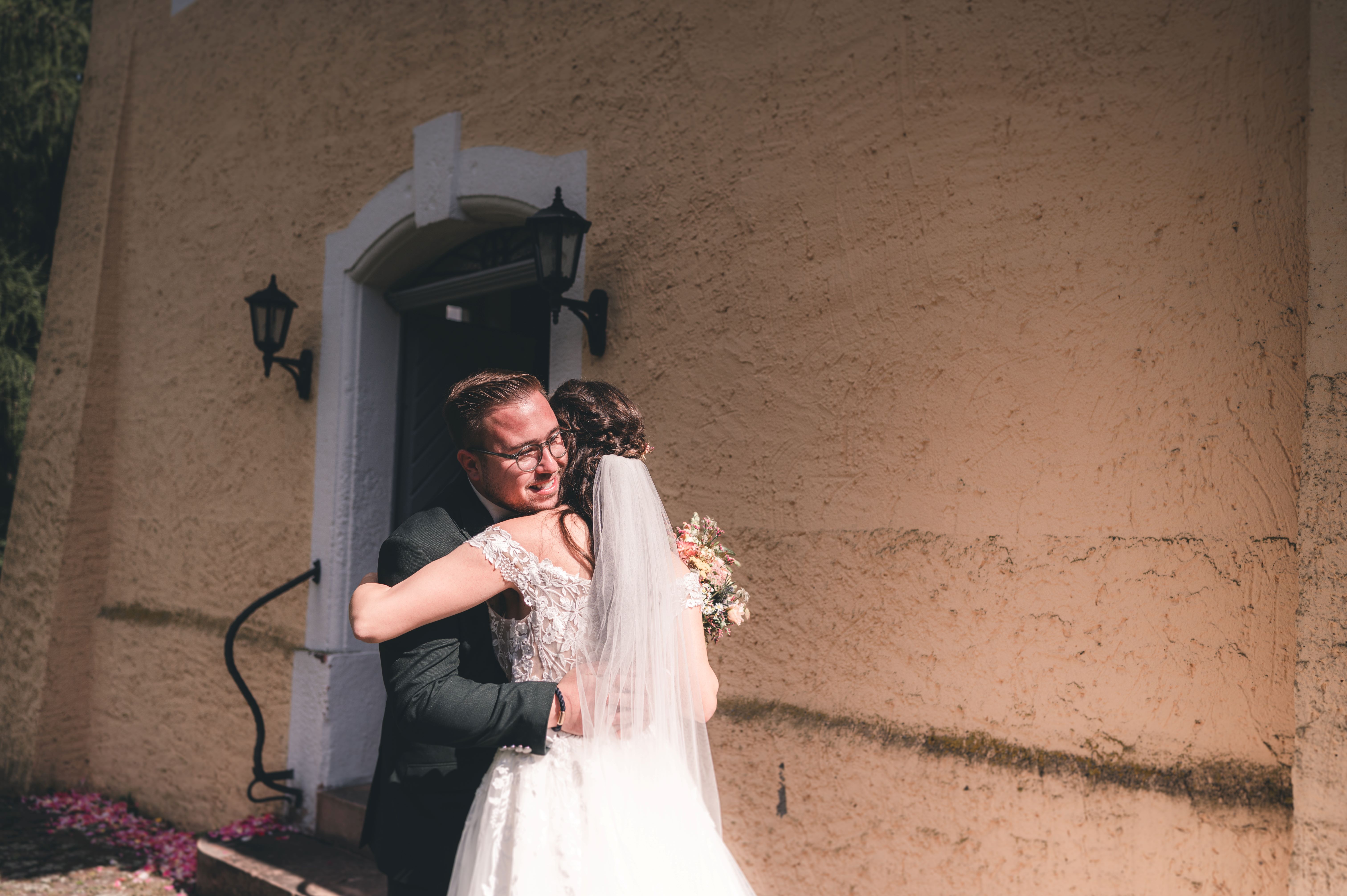 Das Brautpaar umarmt sich hochemotional beim First Look direkt vor dem steinernen Eingang der Kirche in Leisnig.