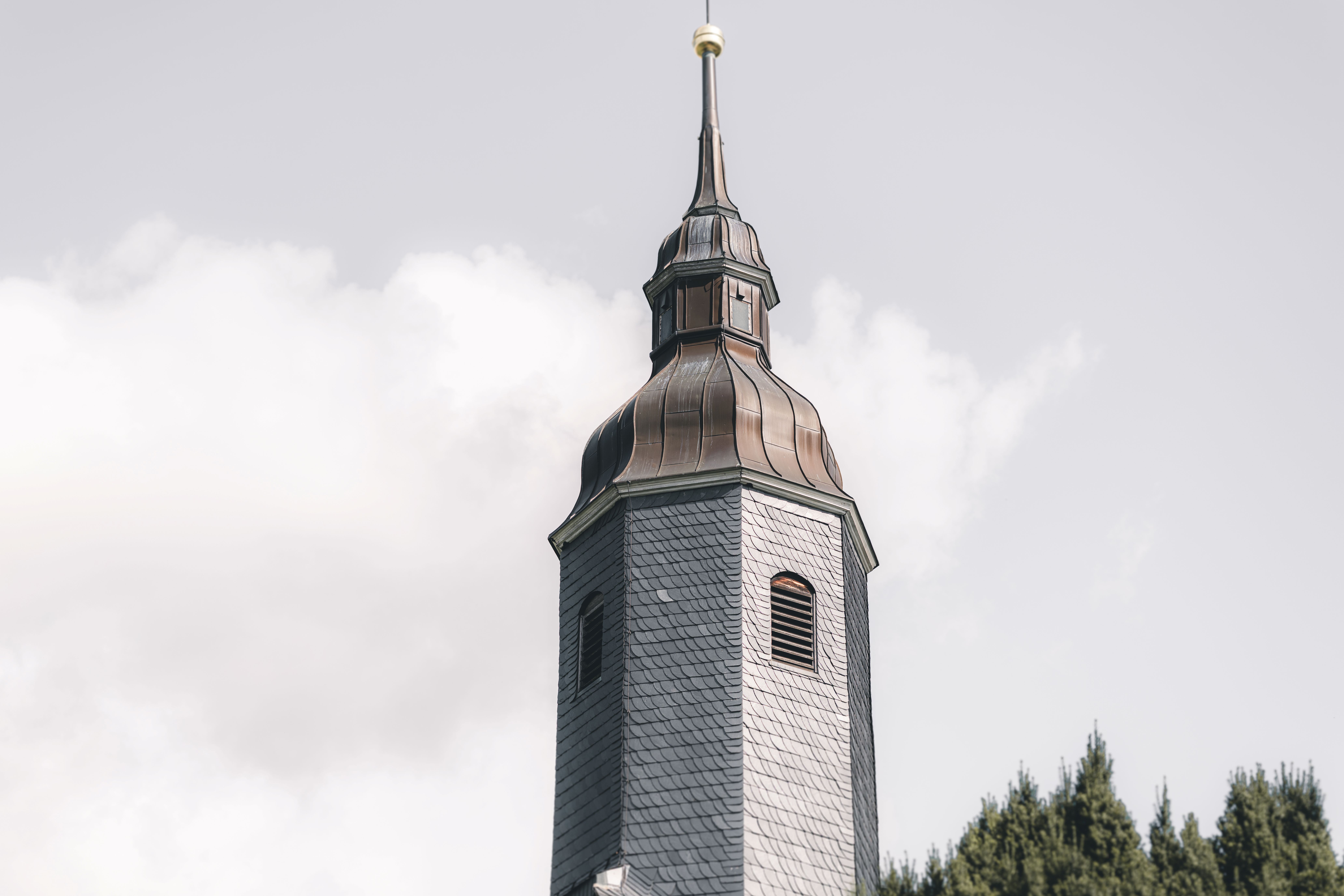 Nahaufnahme eines historischen, schiefergedeckten Kirchturms im Raum Leipzig während einer kirchlichen Trauung im Sommer.