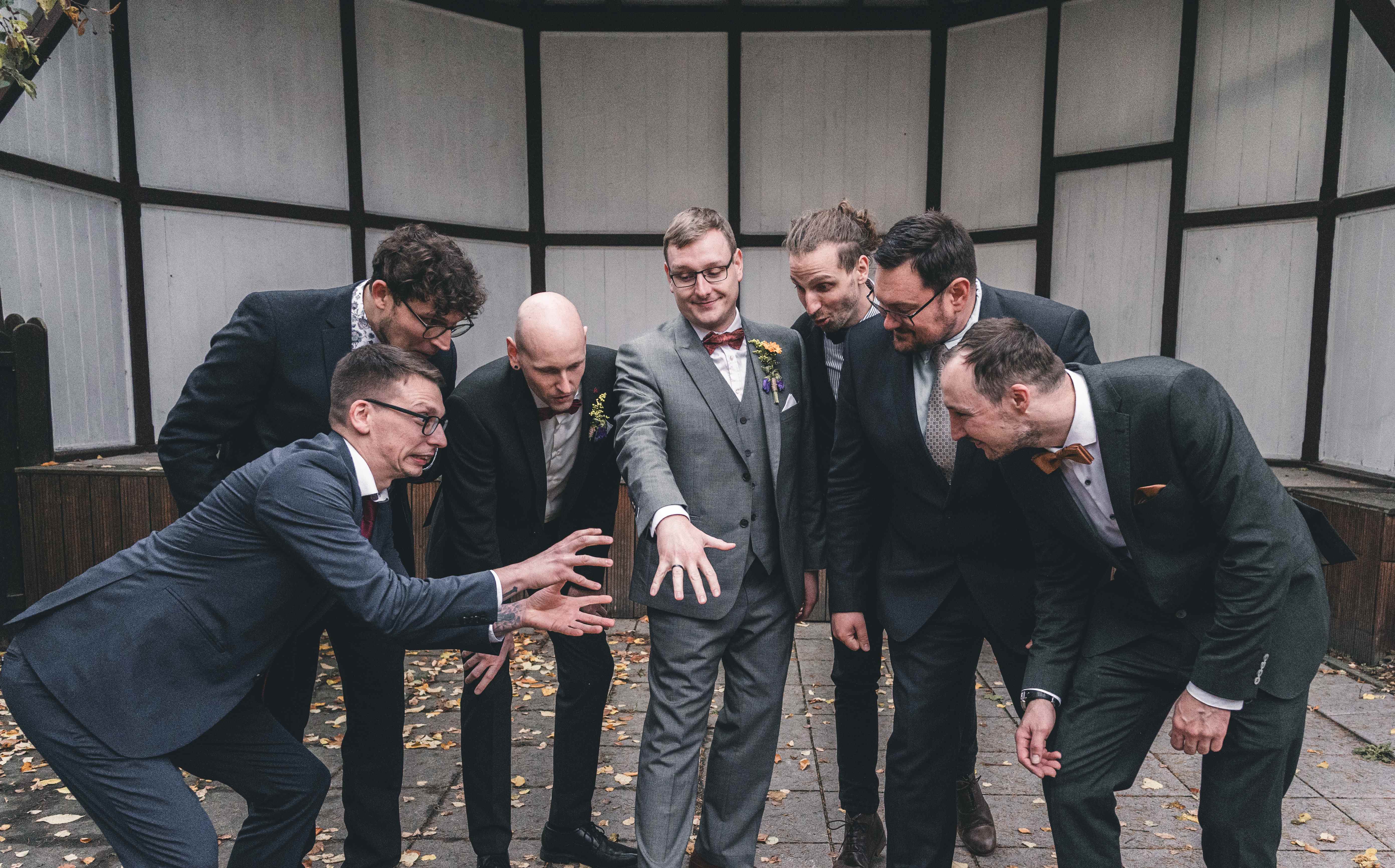 Der Bräutigam zeigt stolz seinen neuen Ehering, während seine Kumpels im Außenbereich der Spitzgrundmühle Coswig humorvoll und schockiert reagieren.