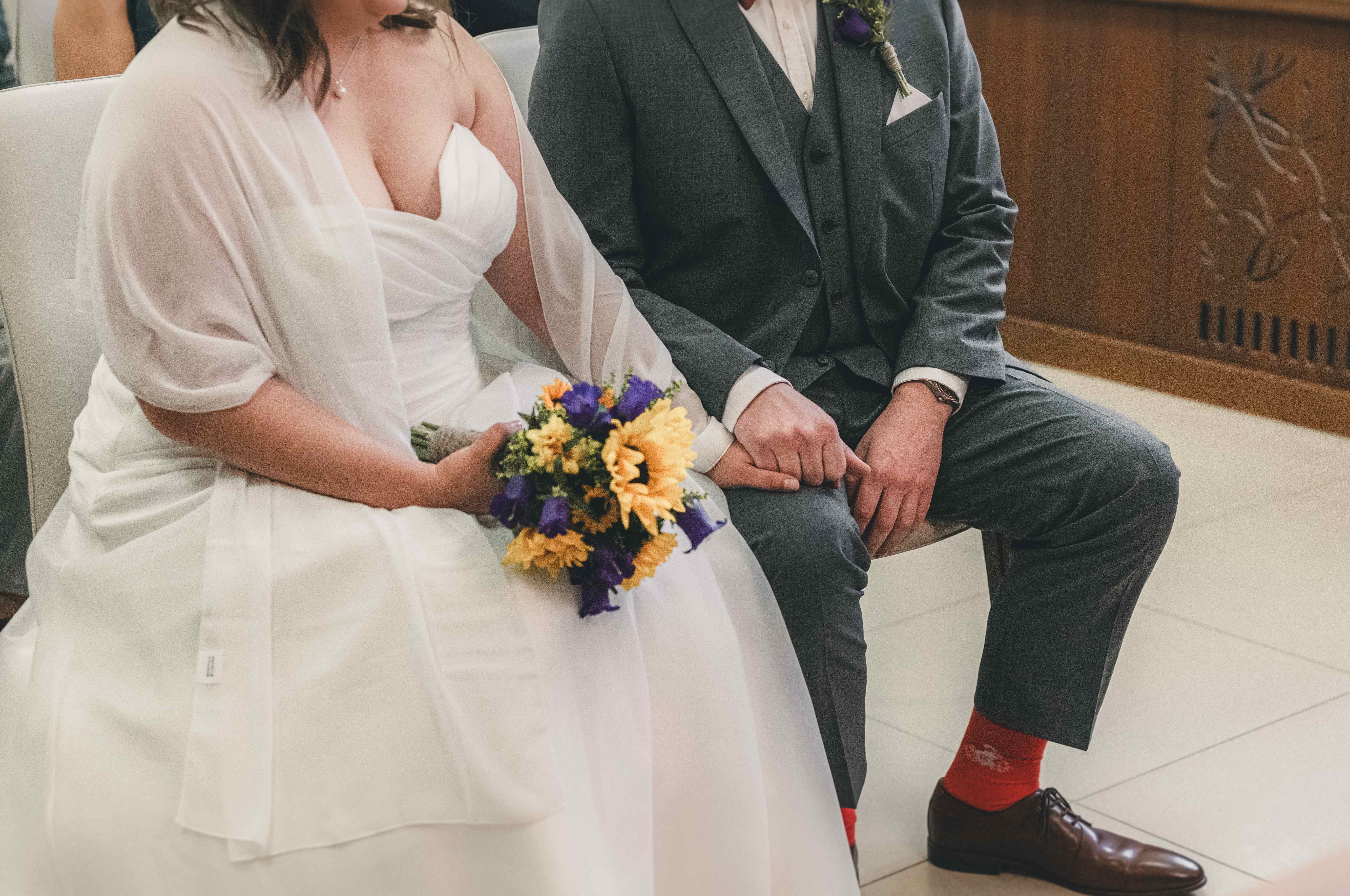 Detailaufnahme des Brautpaares, das während der Trauung im Standesamt Radebeul Hand in Hand sitzt; der Bräutigam trägt rote Socken.