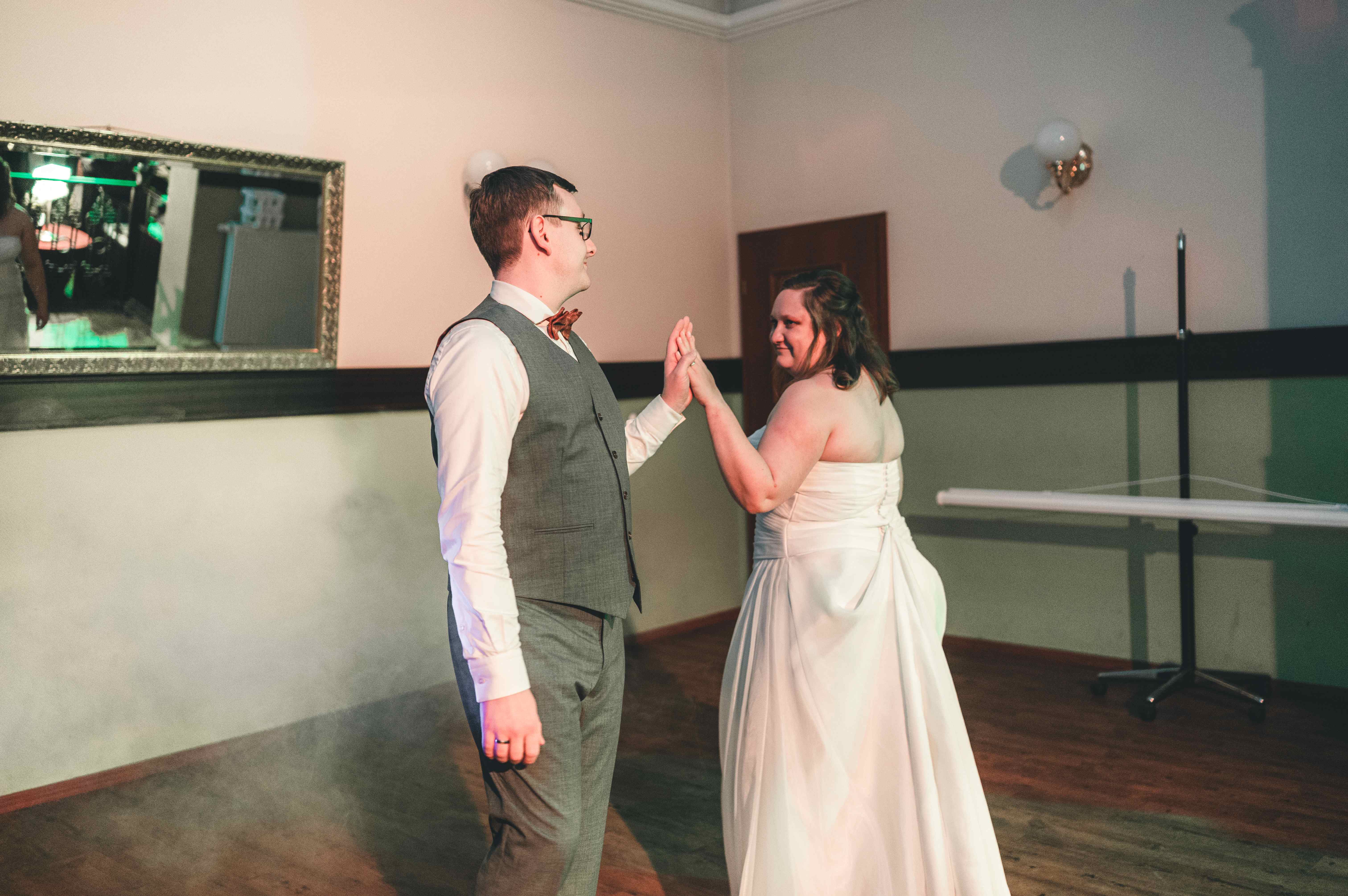 Braut und Bräutigam halten sich an den Händen beim romantischen Hochzeitstanz im Festsaal in Coswig bei Dresden.