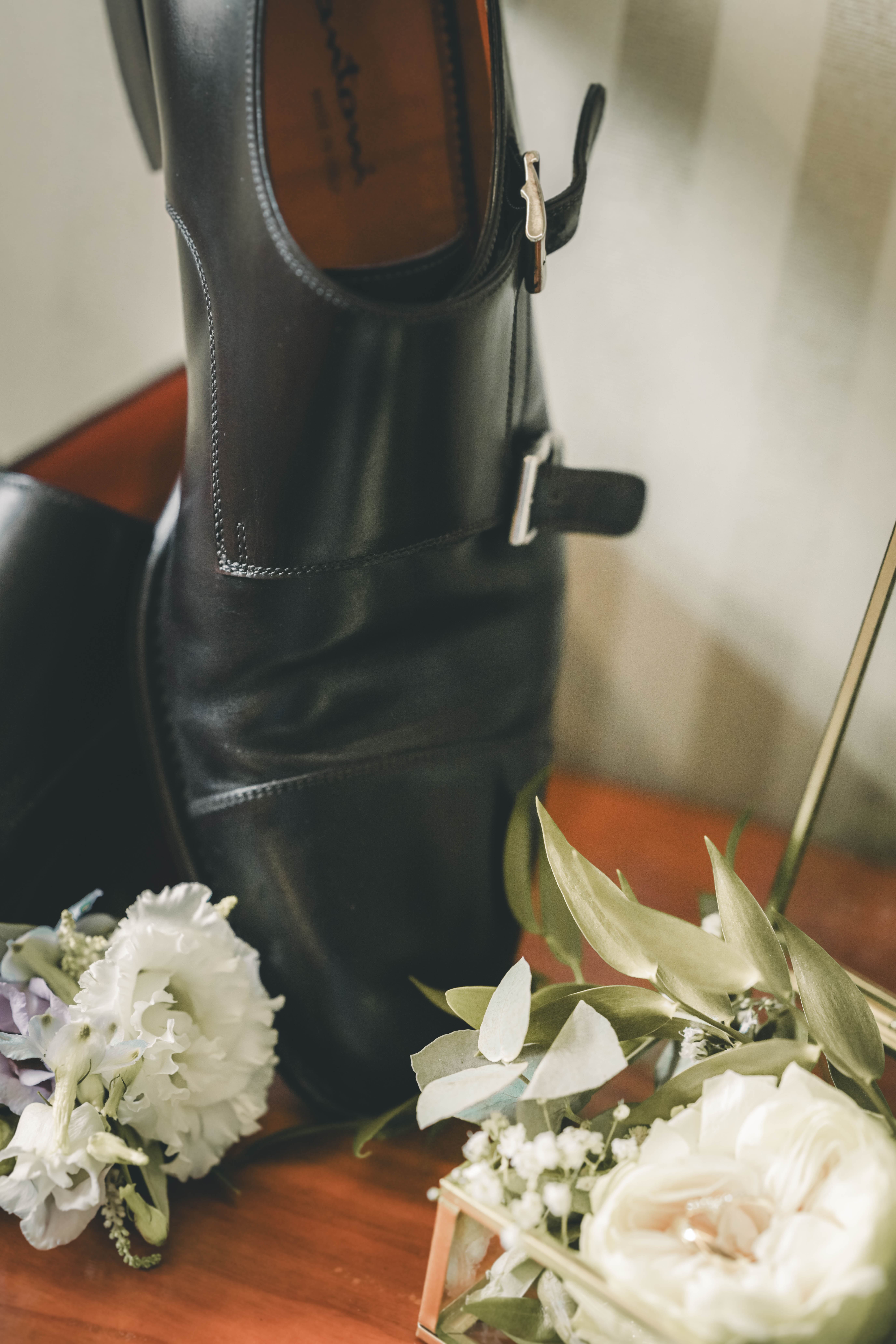 Eleganter schwarzer Santoni-Monkstrap-Schuh mit Boutonnière und weißen Rosen in einer Glasschatulle im Magdalenengut Erfurt.