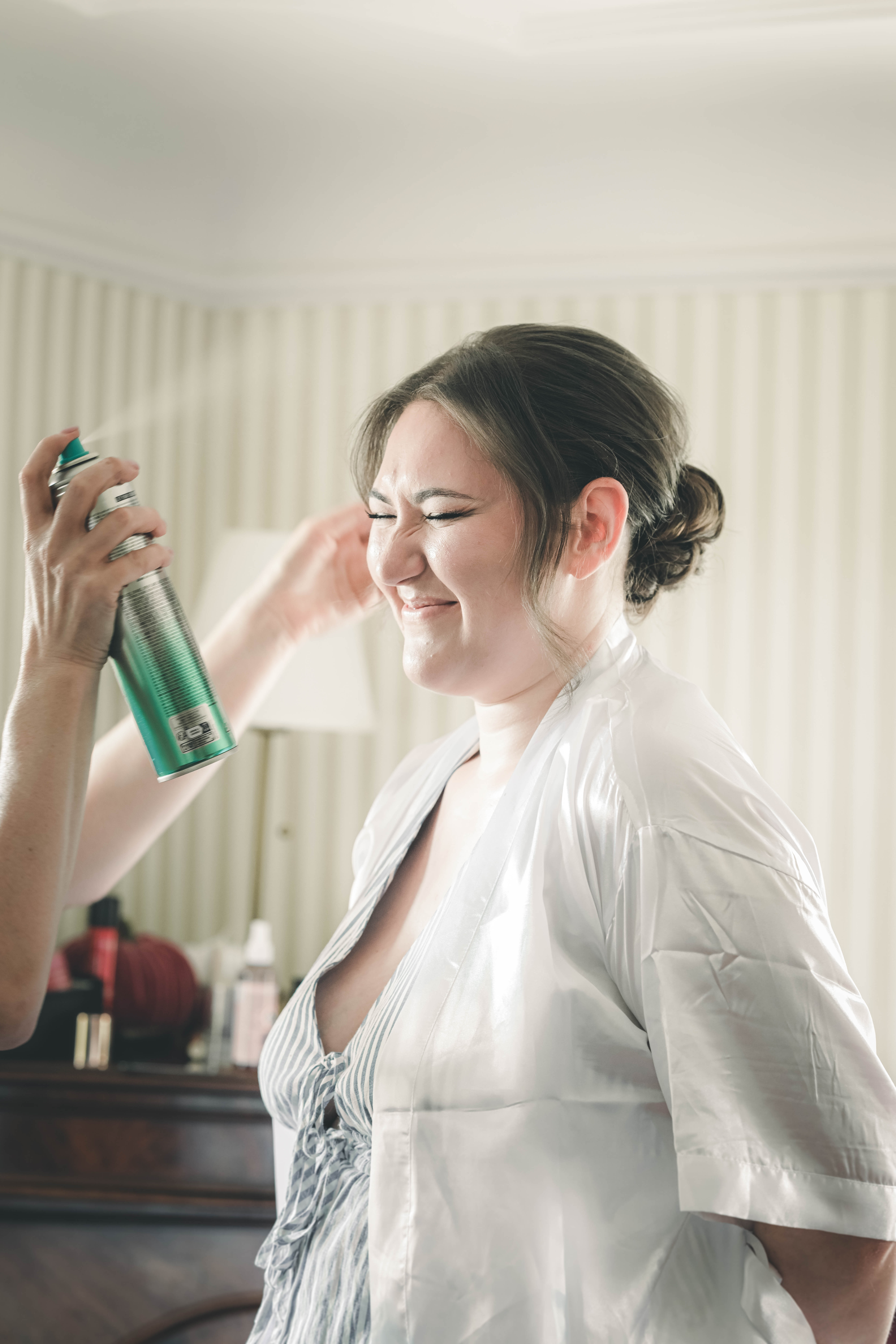 Die Braut schließt lachend die Augen, während ihre Brautfrisur im Magdalenengut Erfurt mit Haarspray fixiert wird.