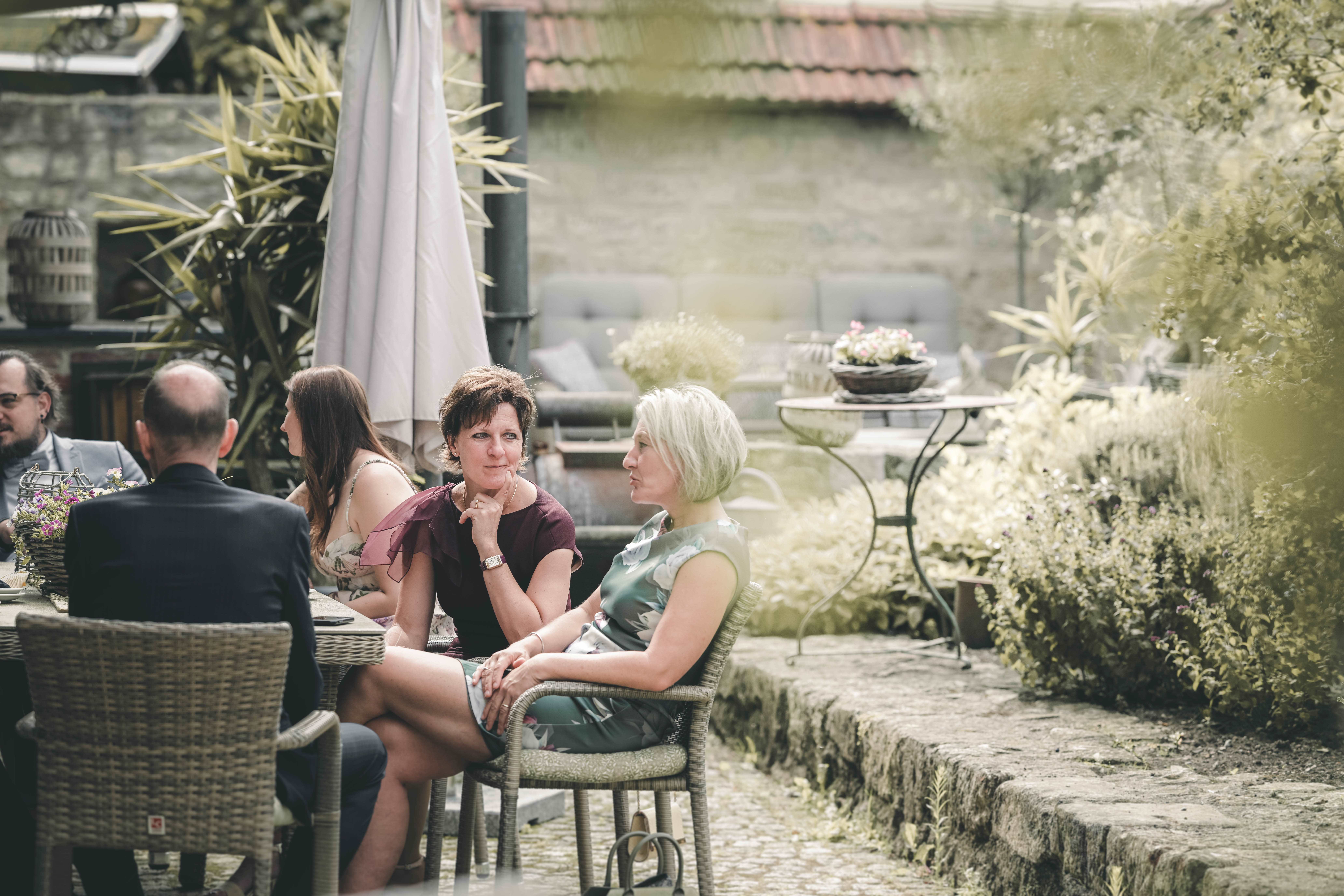 Hochzeitsgäste sitzen entspannt an Rattanmöbeln auf der Terrasse des Magdalenenguts Erfurt und genießen Kaffee und Kuchen.