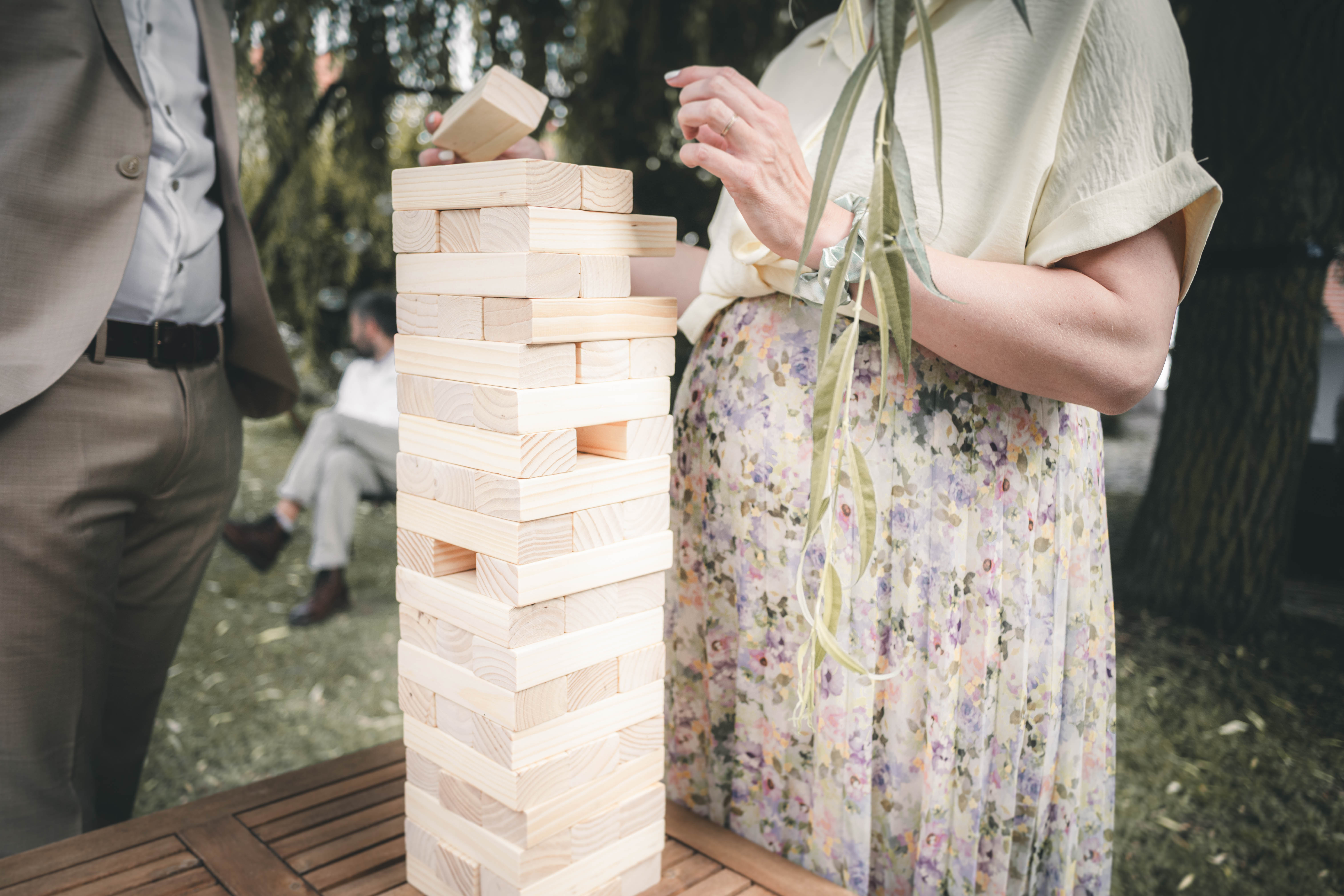 Hochzeitsgäste spielen konzentriert mit einem großen Holzturm aus Bauklötzen auf einem Gartentisch im Magdalenengut Erfurt.