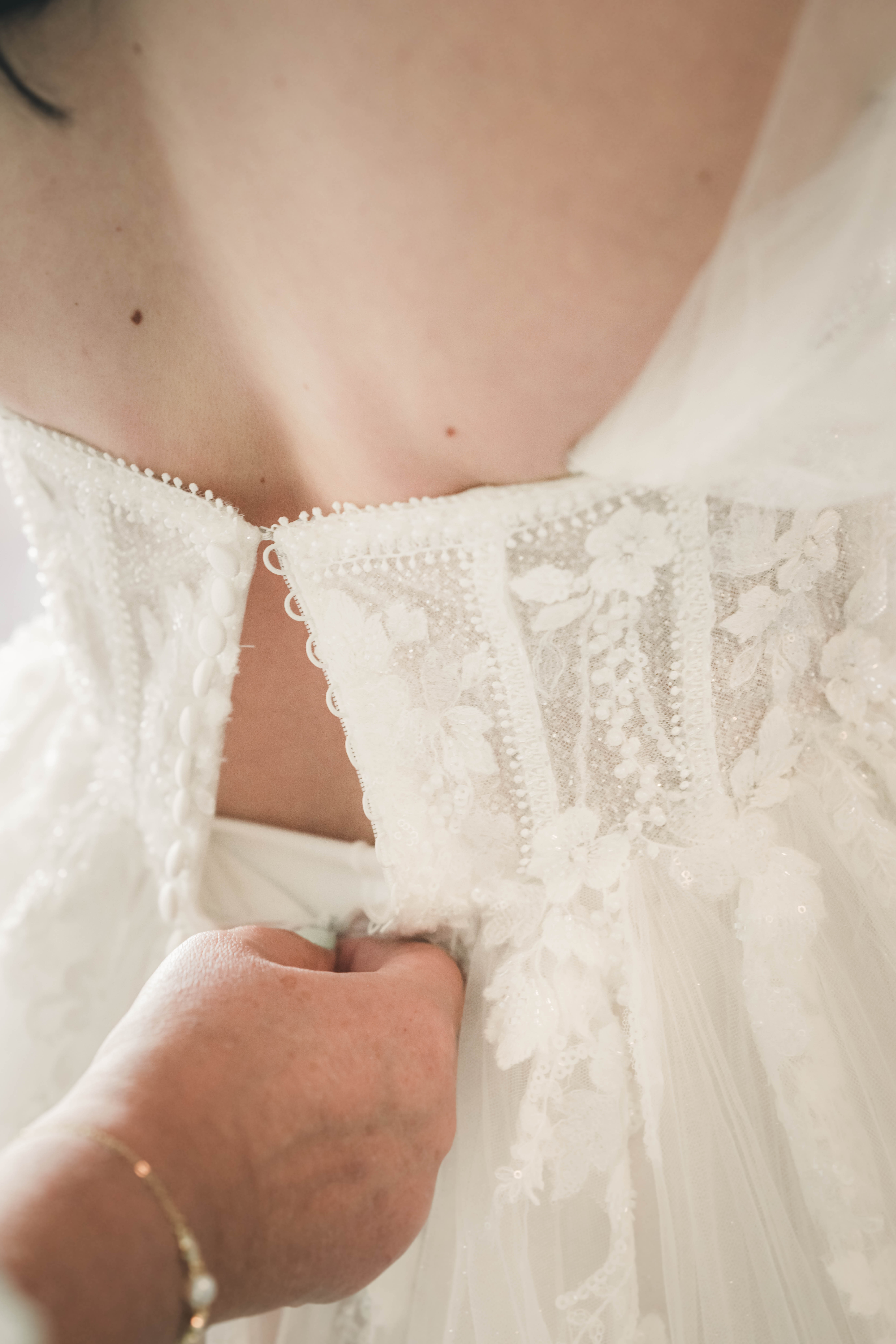 Eine Detailaufnahme von hinten, wie eine Hand die filigrane Knopfleiste des bestickten Hochzeitskleides im Wasserschloss Frankleben schließt.