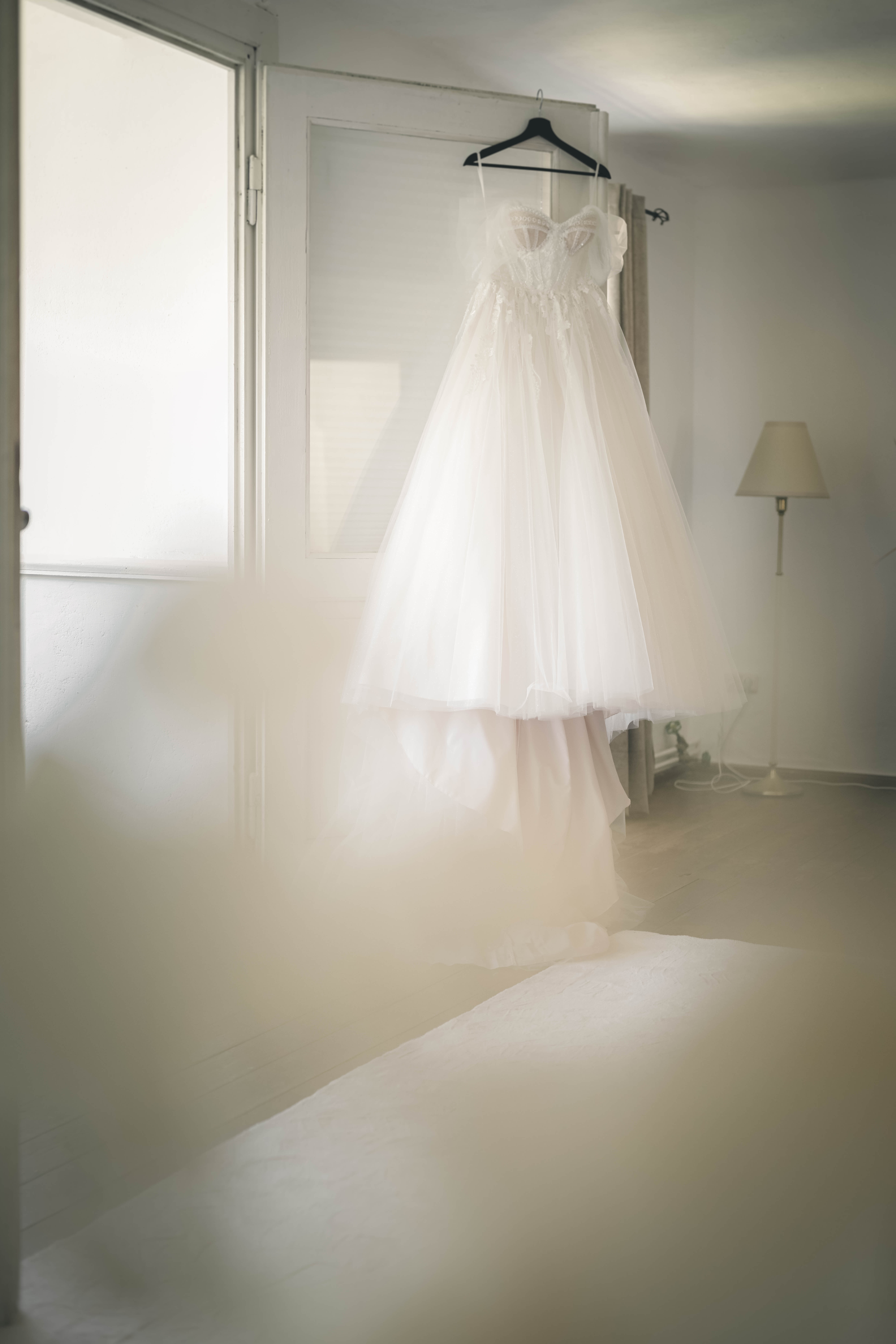 Das weiße, ausladende Brautkleid mit feiner Perlen-Corsage und Tüllschleppe hängt elegant an einer weißen Tür im Wasserschloss Frankleben.