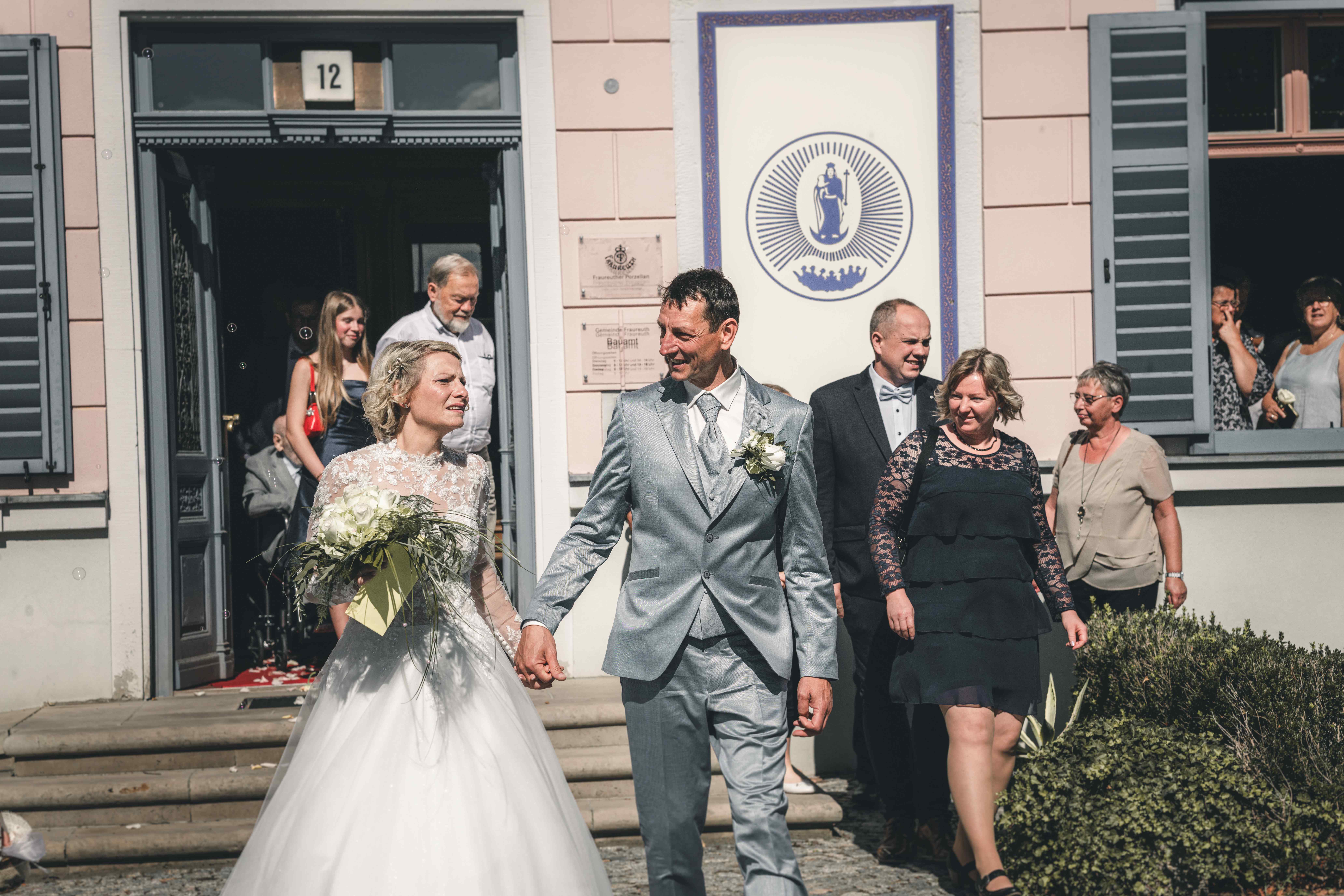 Hand in Hand schreitet das frisch verheiratete Paar die Stufen des rosa Standesamts in Fraureuth hinab, umgeben von Gratulierenden.