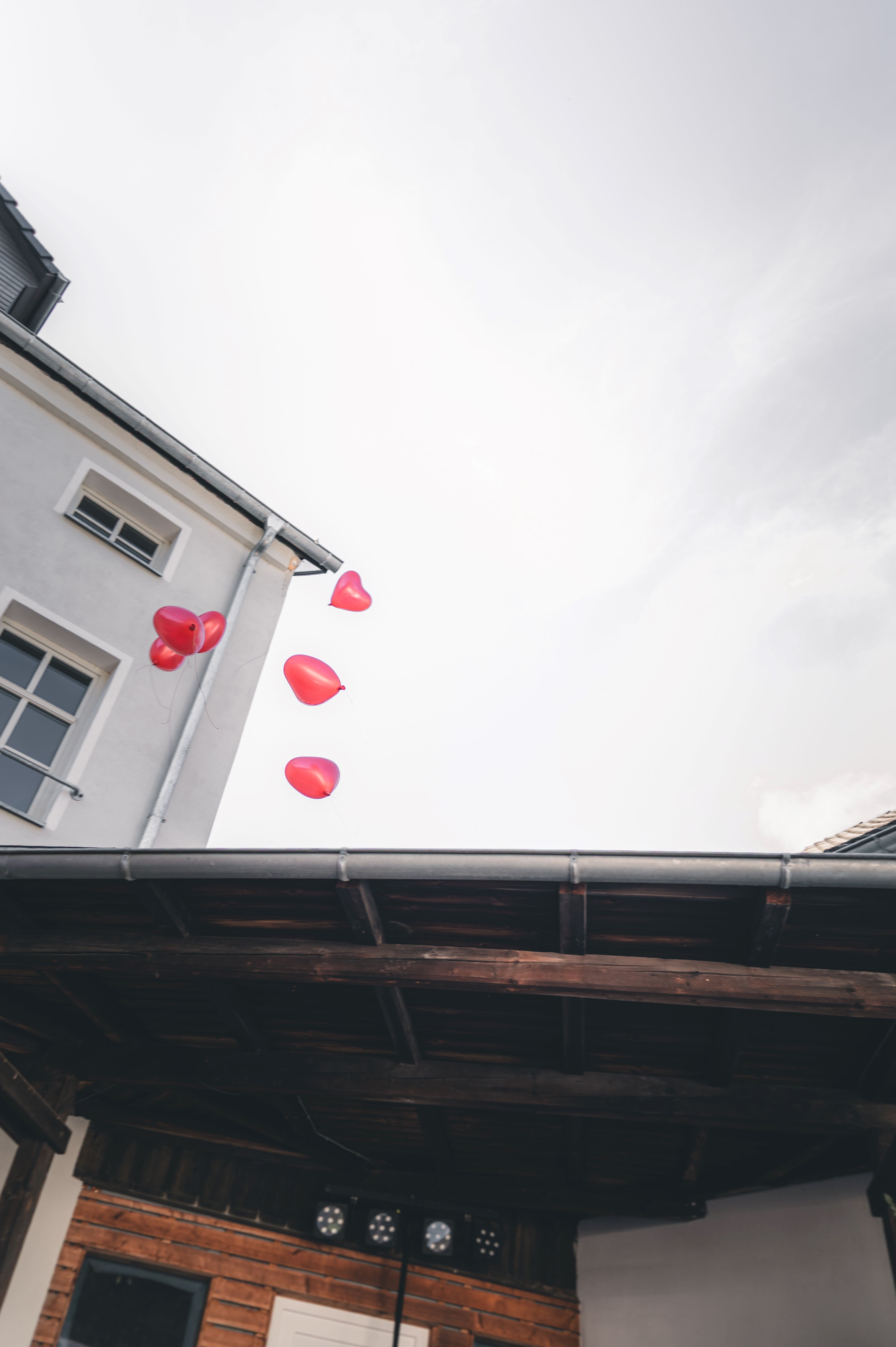 Mehrere rote, herzförmige Luftballons steigen während eines Hochzeitsbrauchs über den Dächern des Gutshofs in Sachsen in den Himmel.