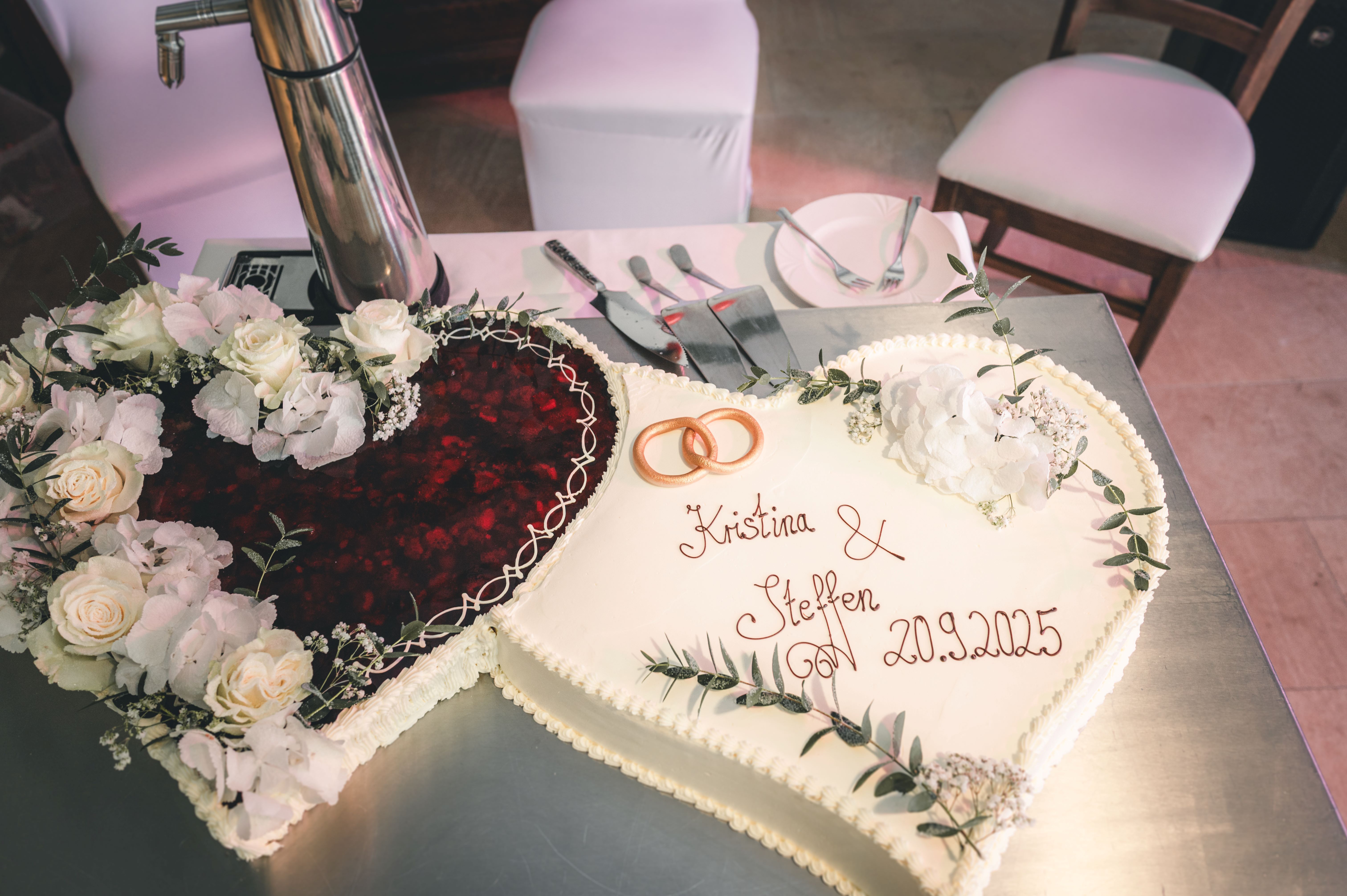 Eine große, doppelherzförmige Hochzeitstorte, garniert mit frischen Erdbeeren, weißen Rosen und den Namen des Brautpaares in Westsachsen.
