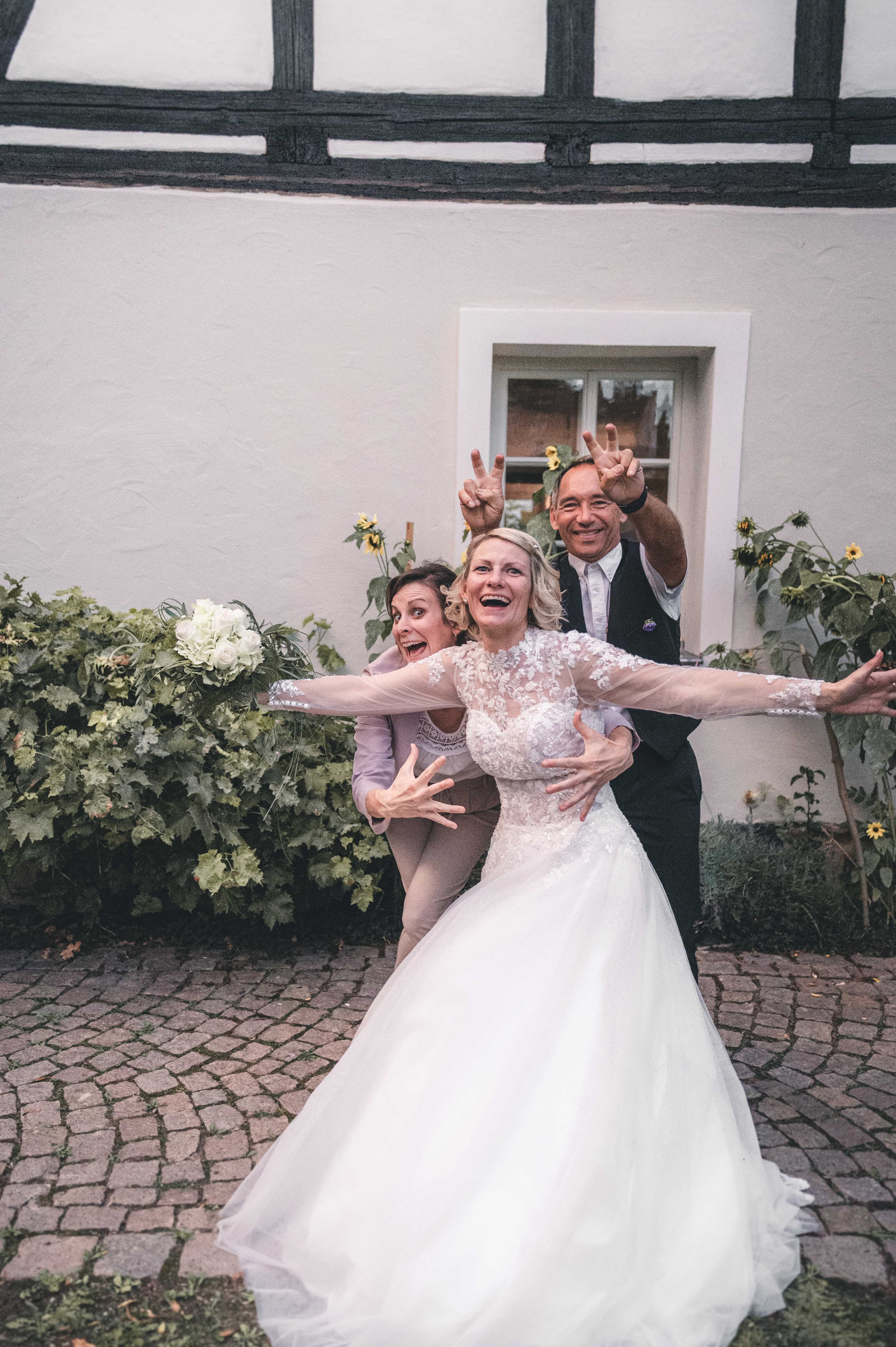 Kristina und Steffen posieren mit weit ausgestreckten Armen und lustigen Grimassen zusammen mit Freunden vor dem Erlebnishof Pleißental.