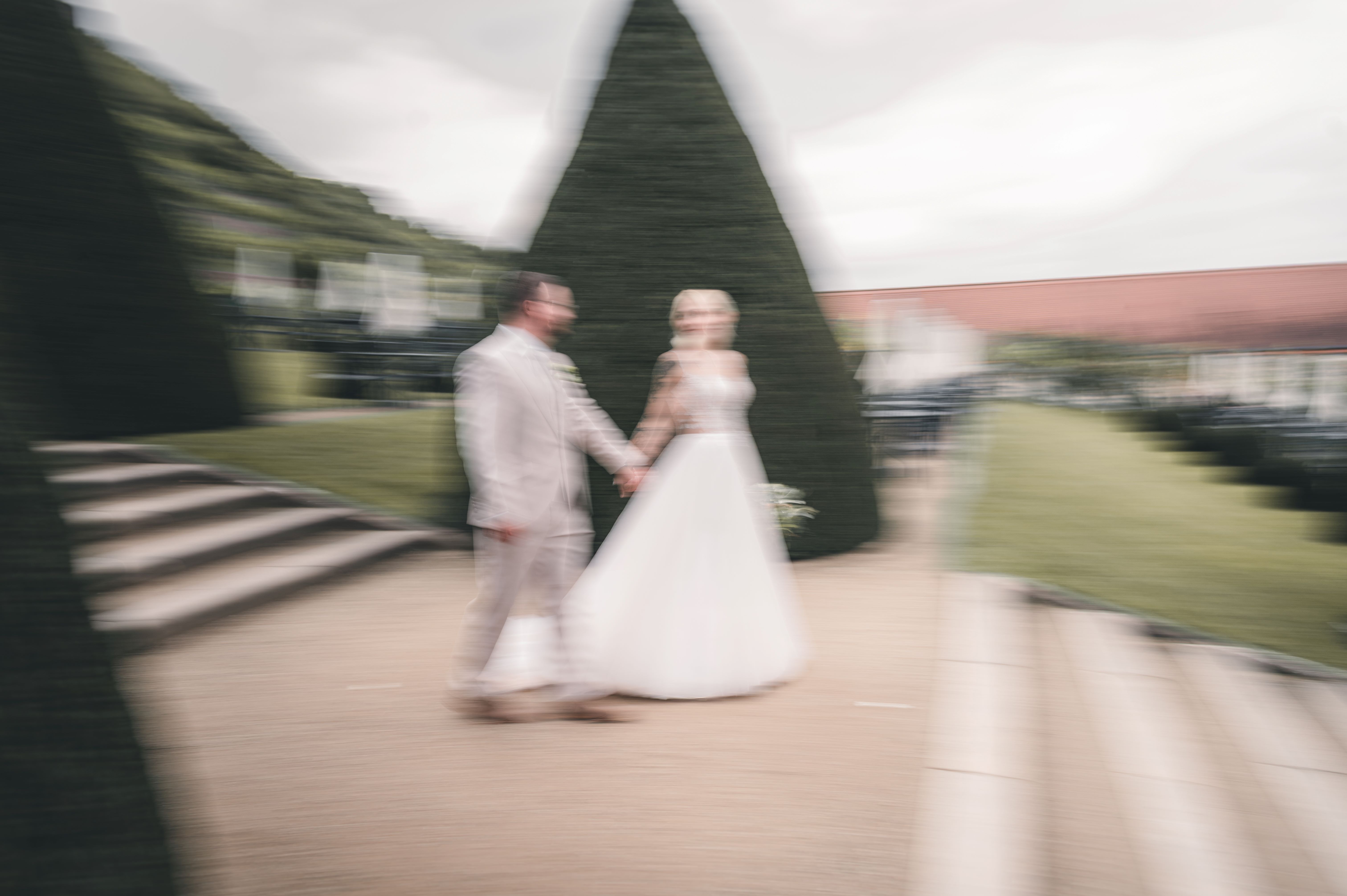Künstlerische Aufnahme mit Bewegungsunschärfe (Motion Blur): Das Brautpaar läuft Hand in Hand gut gelaunt durch das grüne Hecken-Labyrinth im Schlossgarten.