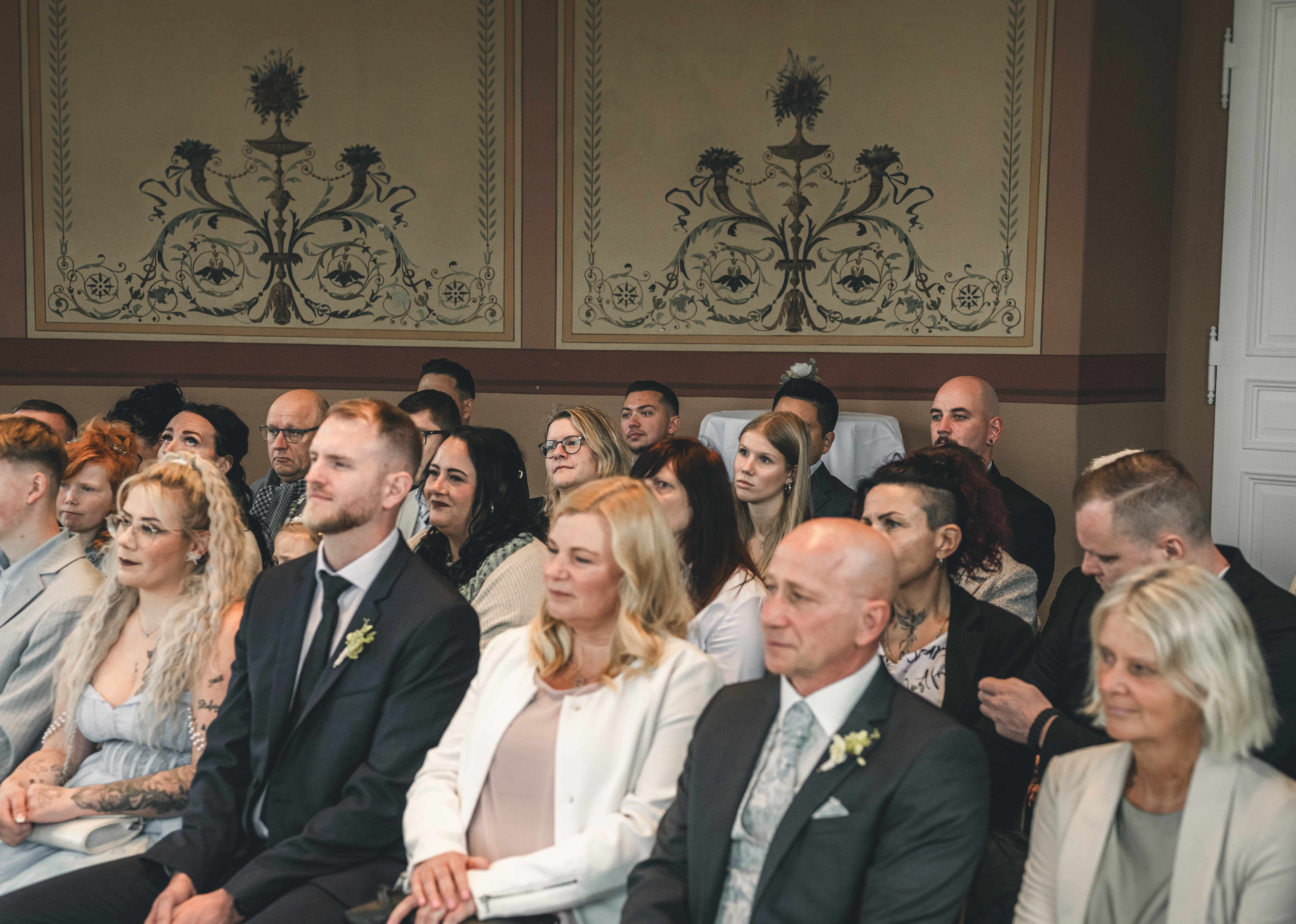Die Hochzeitsgäste und engsten Verwandten sitzen aufmerksam und sichtlich gerührt in den Sitzreihen während der feierlichen Hochzeitszeremonie.