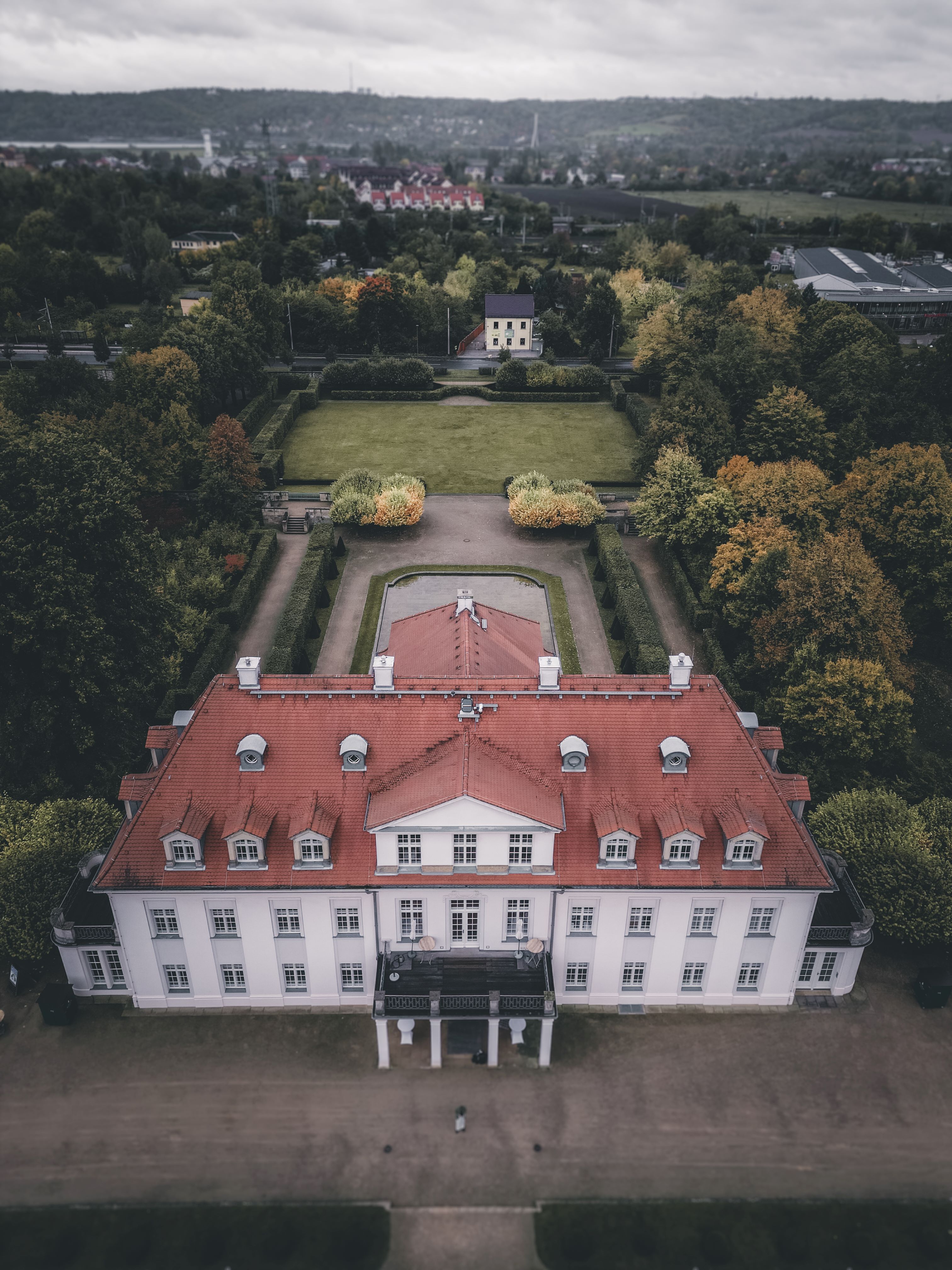 Eine spektakuläre, gerade Drohnen-Luftaufnahme von Schloss Wackerbarth mit Blick auf das rote Dach, den symmetrischen Barockgarten und die herbstlichen Bäume.