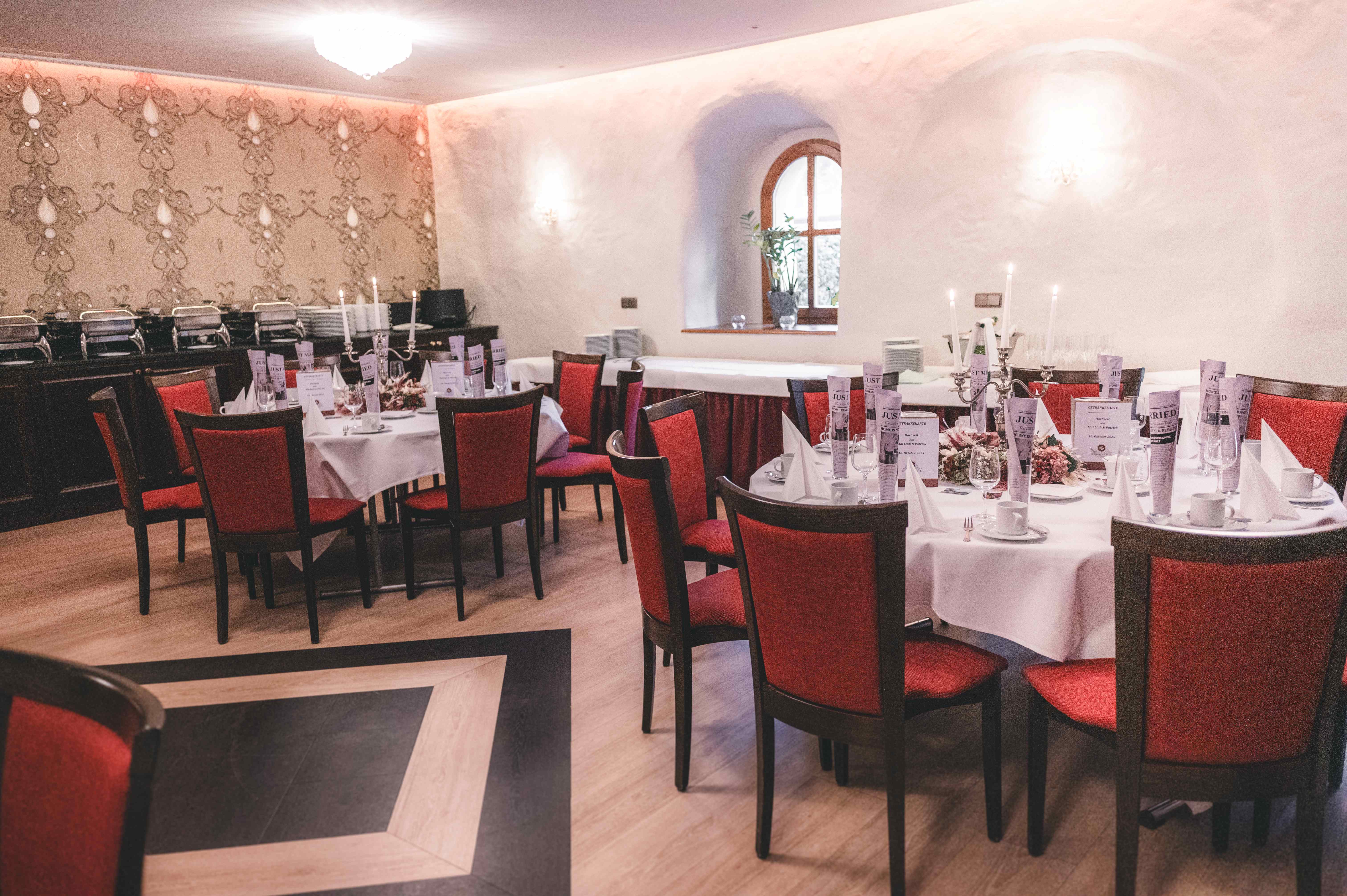Ein elegant dekorierter Hochzeitssaal mit runden Tischen, roten Stühlen und weißen Tischtüchern für eine Ganztagesreportage in Sachsen.
