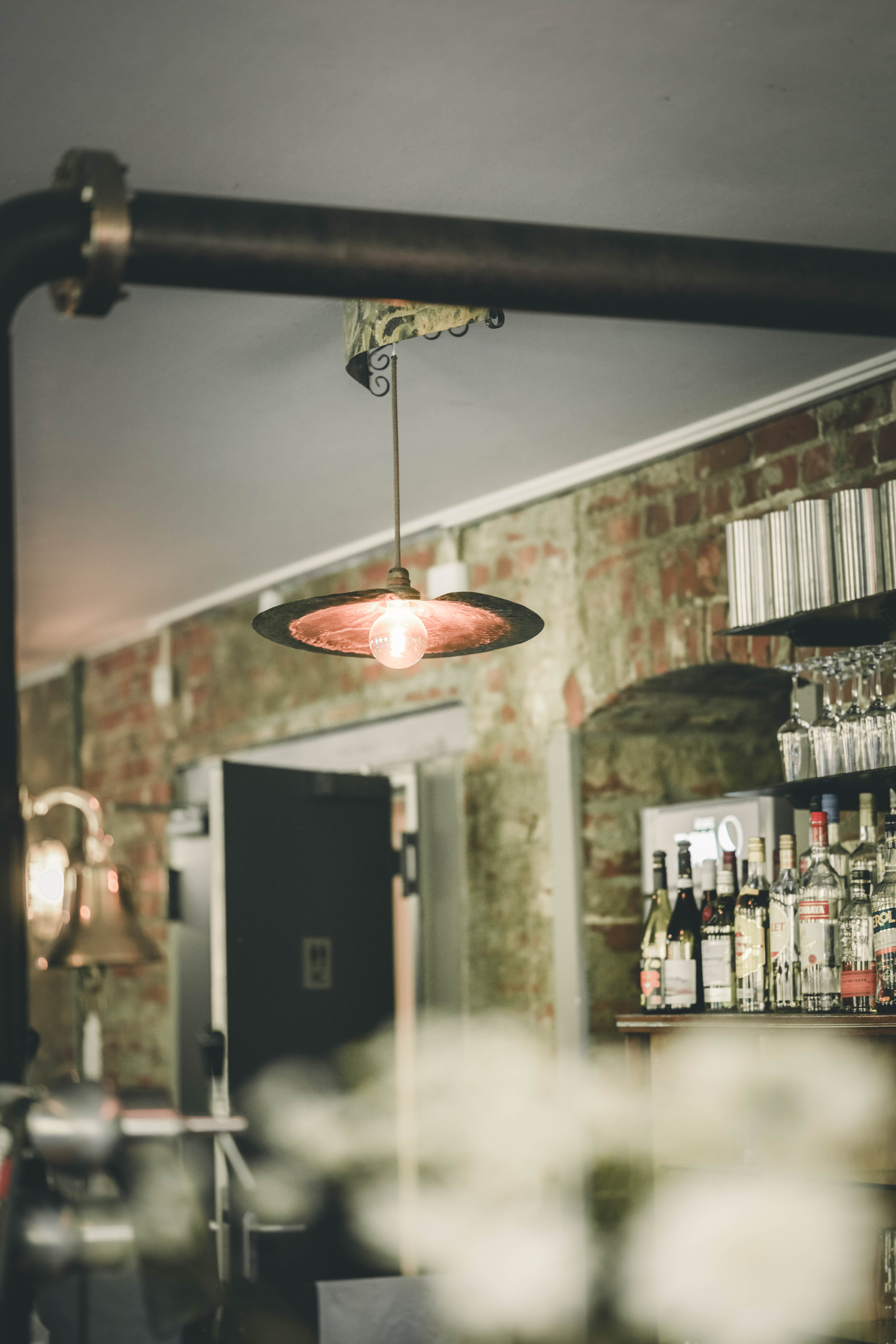Eine brennende Glühbirne unter einer rustikalen Metalllampe sorgt für stimmungsvolles Licht vor der unverputzten Ziegelwand der Bar im Mörtelwerk Leipzig.