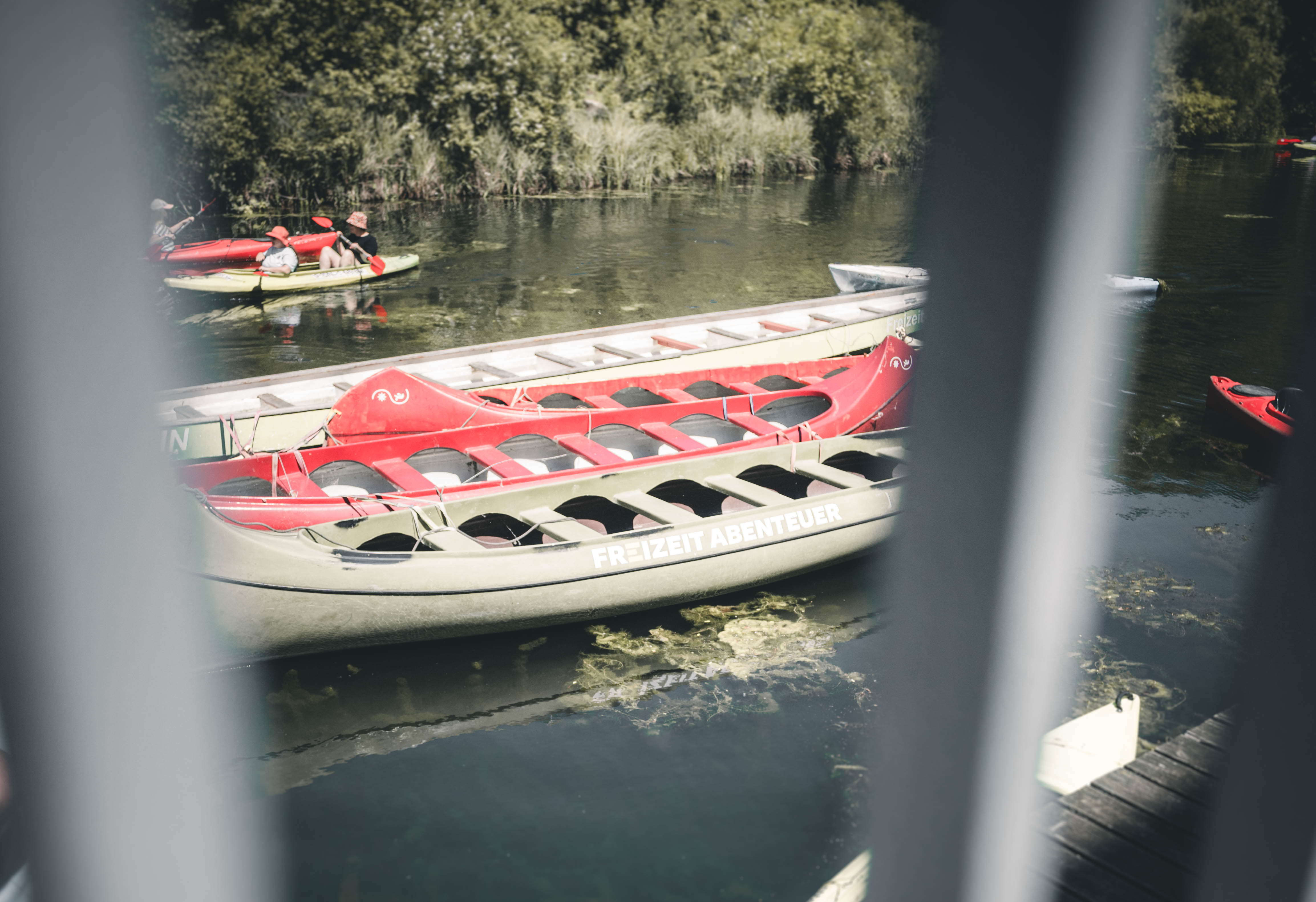 Ein Blick durch das Geländer auf die roten und grünen Kanus, die am Steg des Mörtelwerks auf dem Karl-Heine-Kanal in Leipzig liegen.