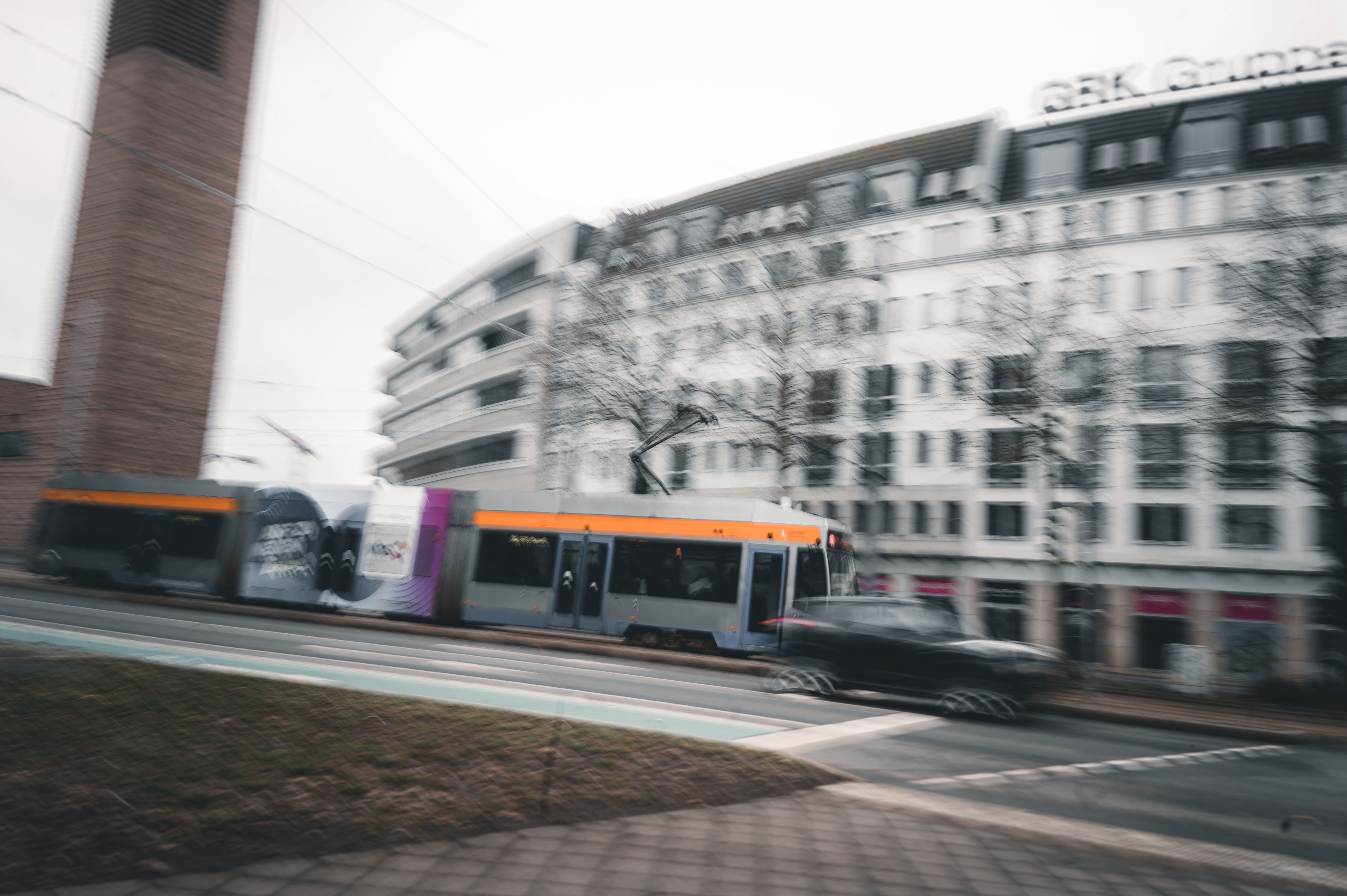 Eine dynamische Mitzieher-Aufnahme einer Leipziger Straßenbahn in der Innenstadt vor moderner Architektur, die den urbanen Vibe einer Stadthochzeit einfängt.