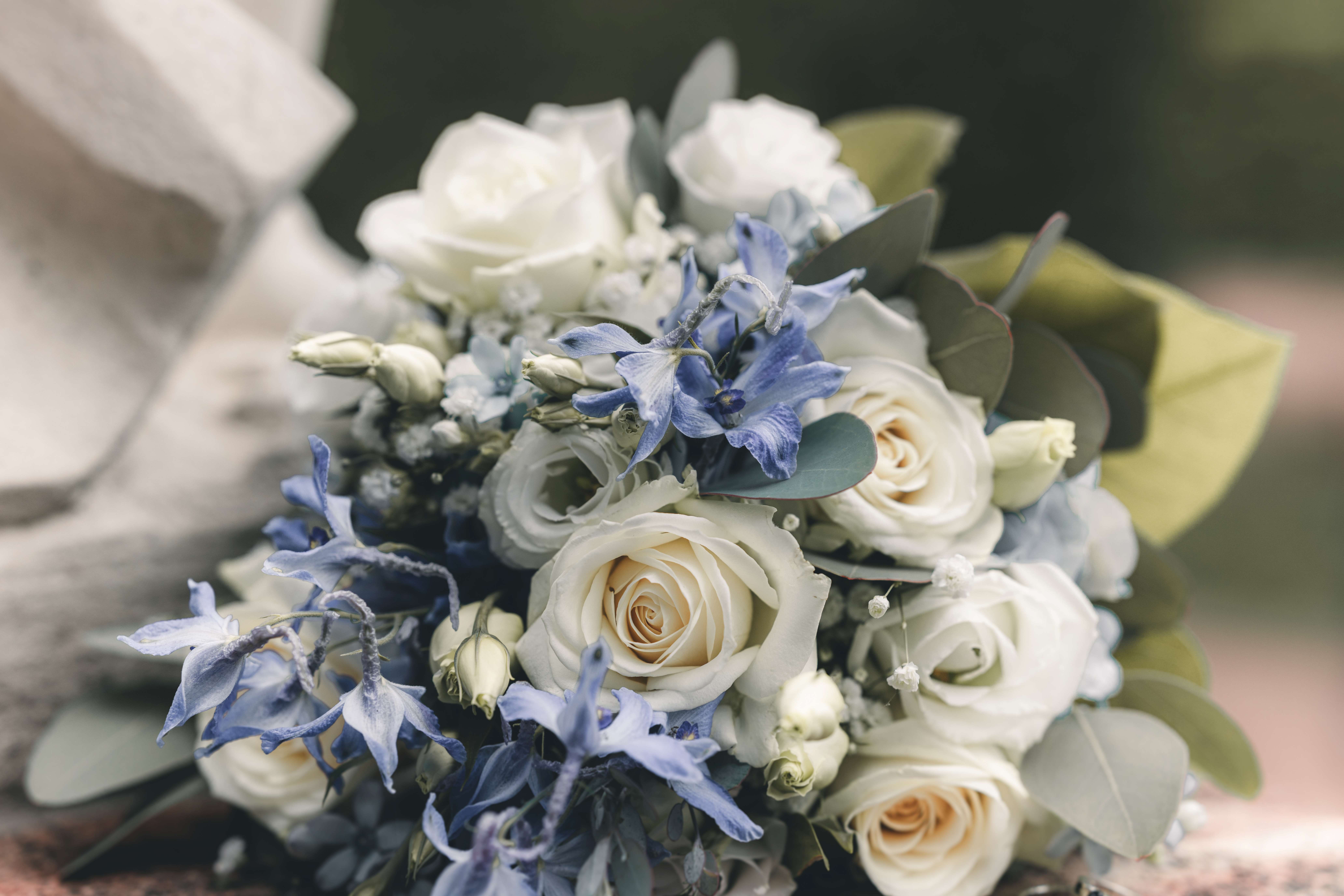 Nahaufnahme des eleganten Brautstraußes aus weißen Rosen und blauen Blüten, arrangiert auf einem historischen Steinsockel im Raum Chemnitz.