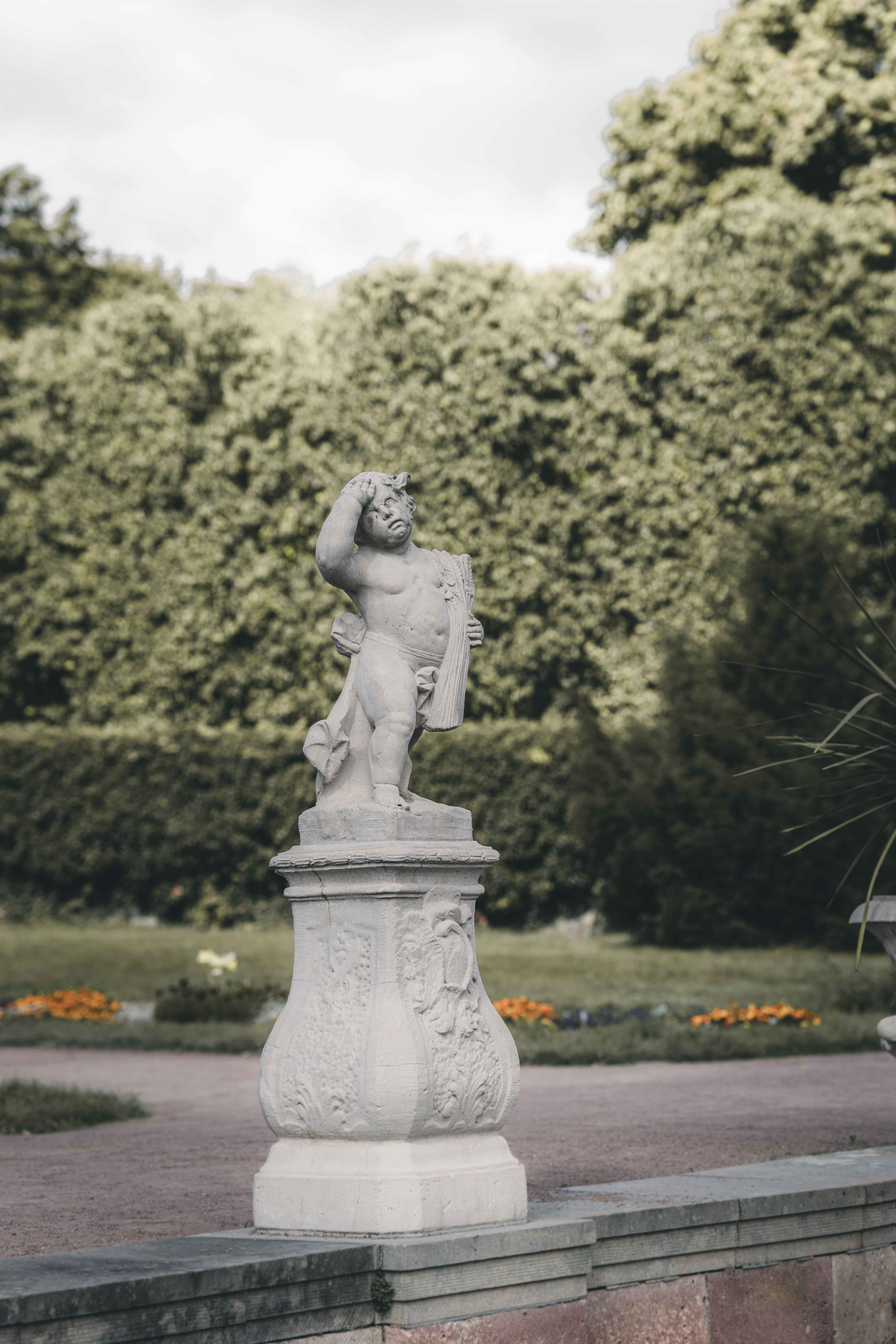 Eine historische Barock-Skulptur aus Sandstein auf einem verzierten Sockel im gepflegten Park von Schloss Lichtenwalde bei Chemnitz.