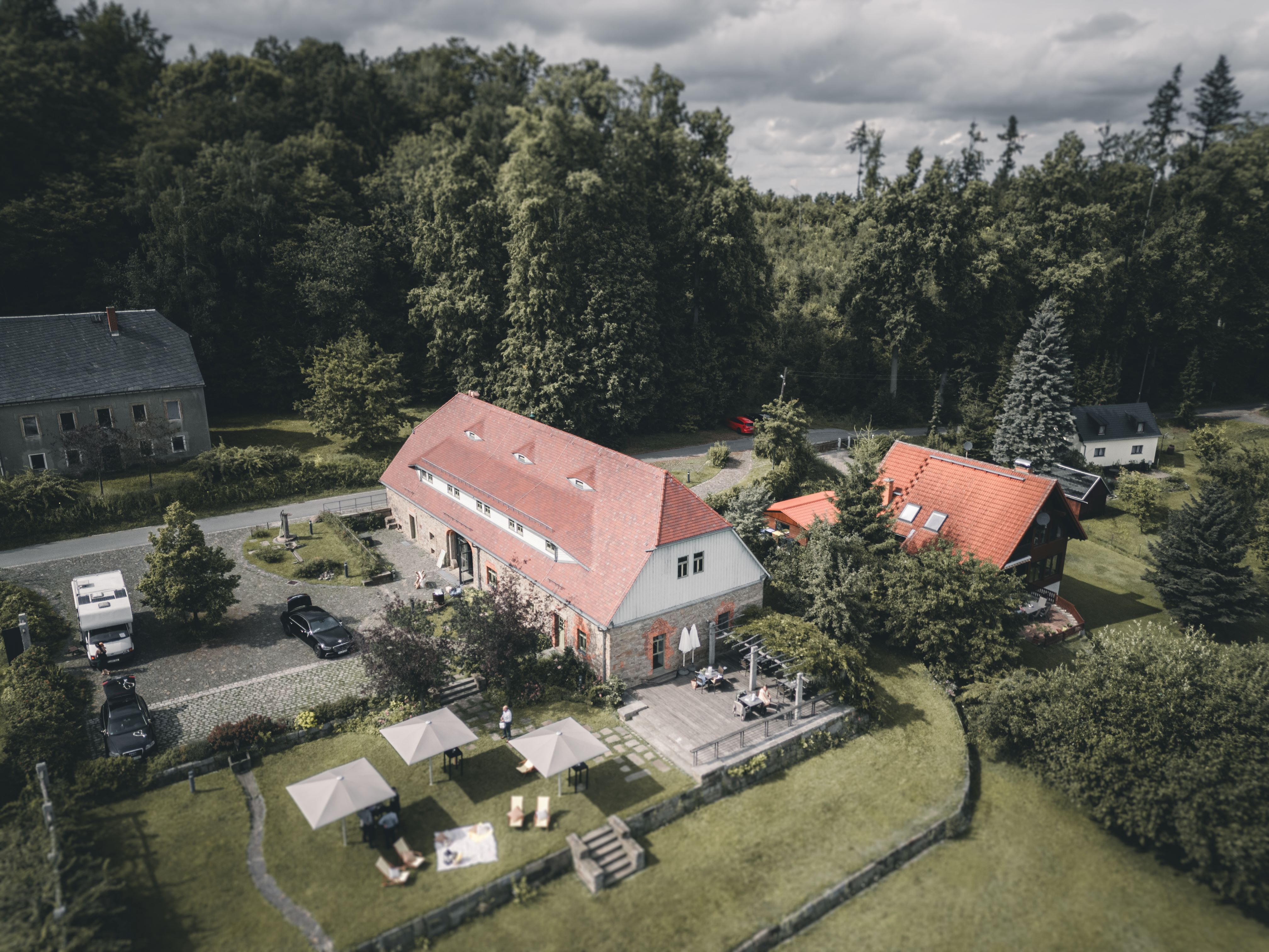 Eine beeindruckende Drohnen-Luftaufnahme des historischen Gebäudekomplexes der Alten Schäferei in Oppach mit ihrer einladenden Festwiese.