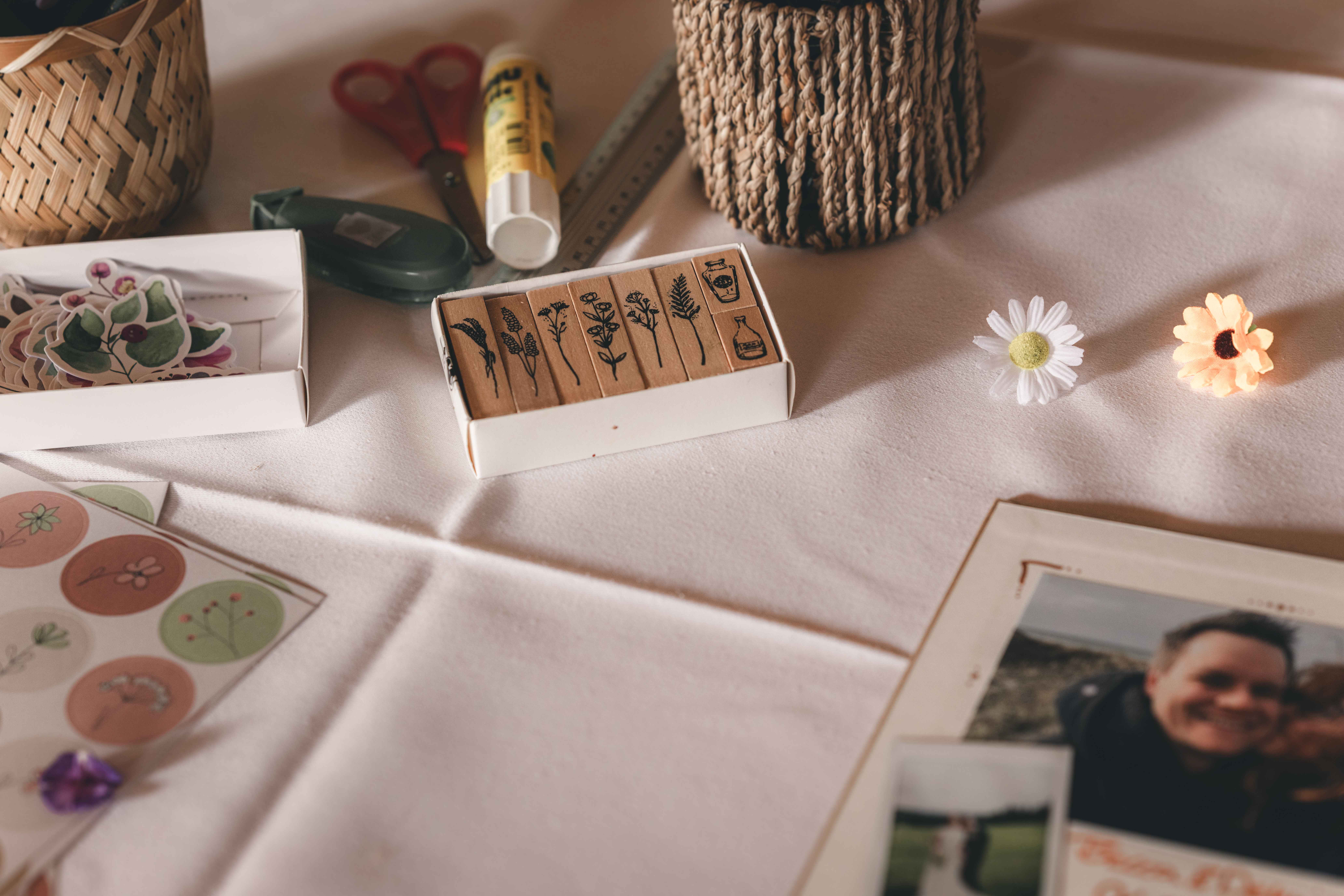 Eine Auswahl an Holzstempeln mit botanischen Motiven, Stickern und Scheren auf einem weißen Tischtuch für die Gestaltung des Gästebuchs.