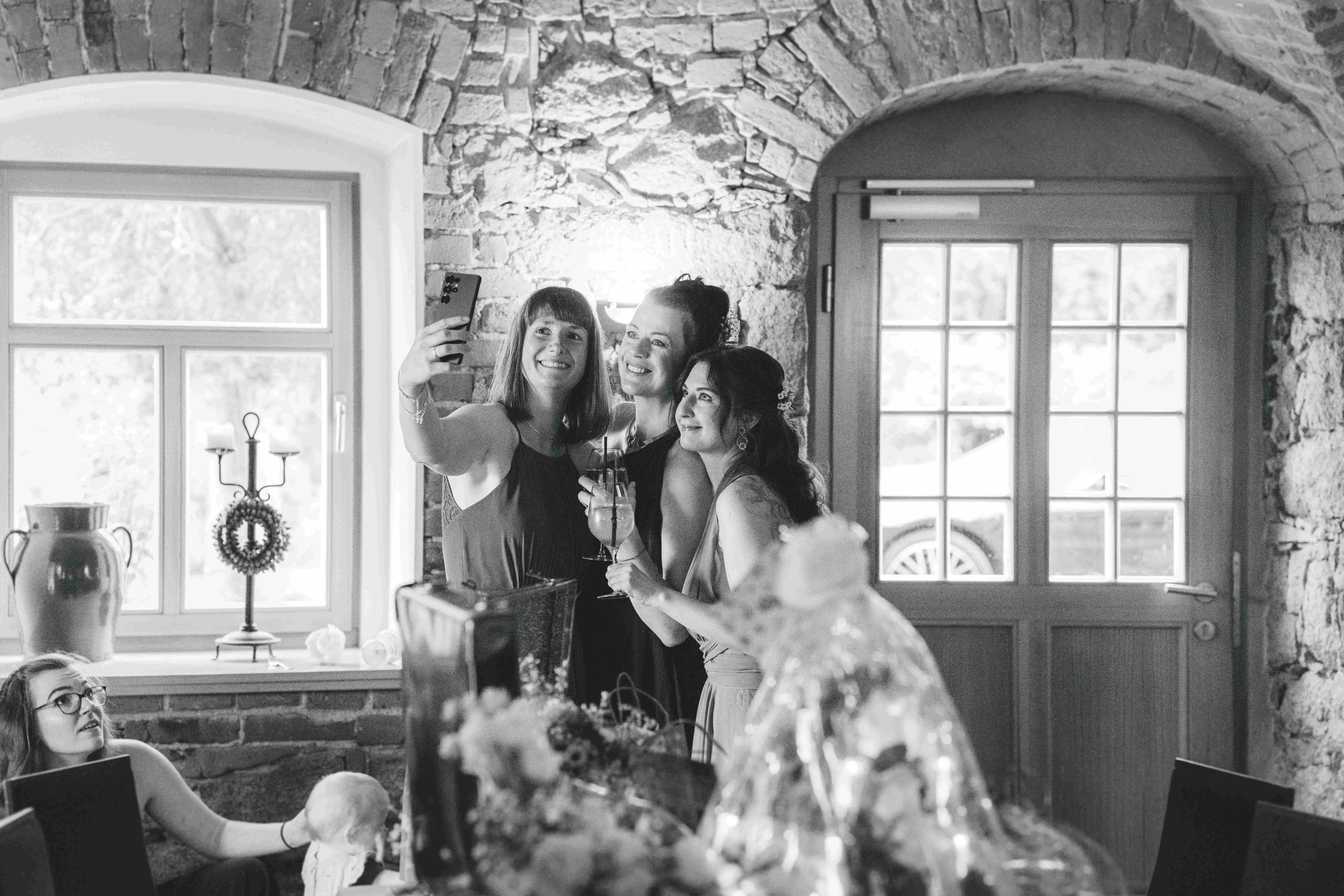 Drei gut gelaunte Hochzeitsgäste machen ein Selfie mit dem Smartphone im historischen Gewölbesaal der Alten Schäferei in Oppach.