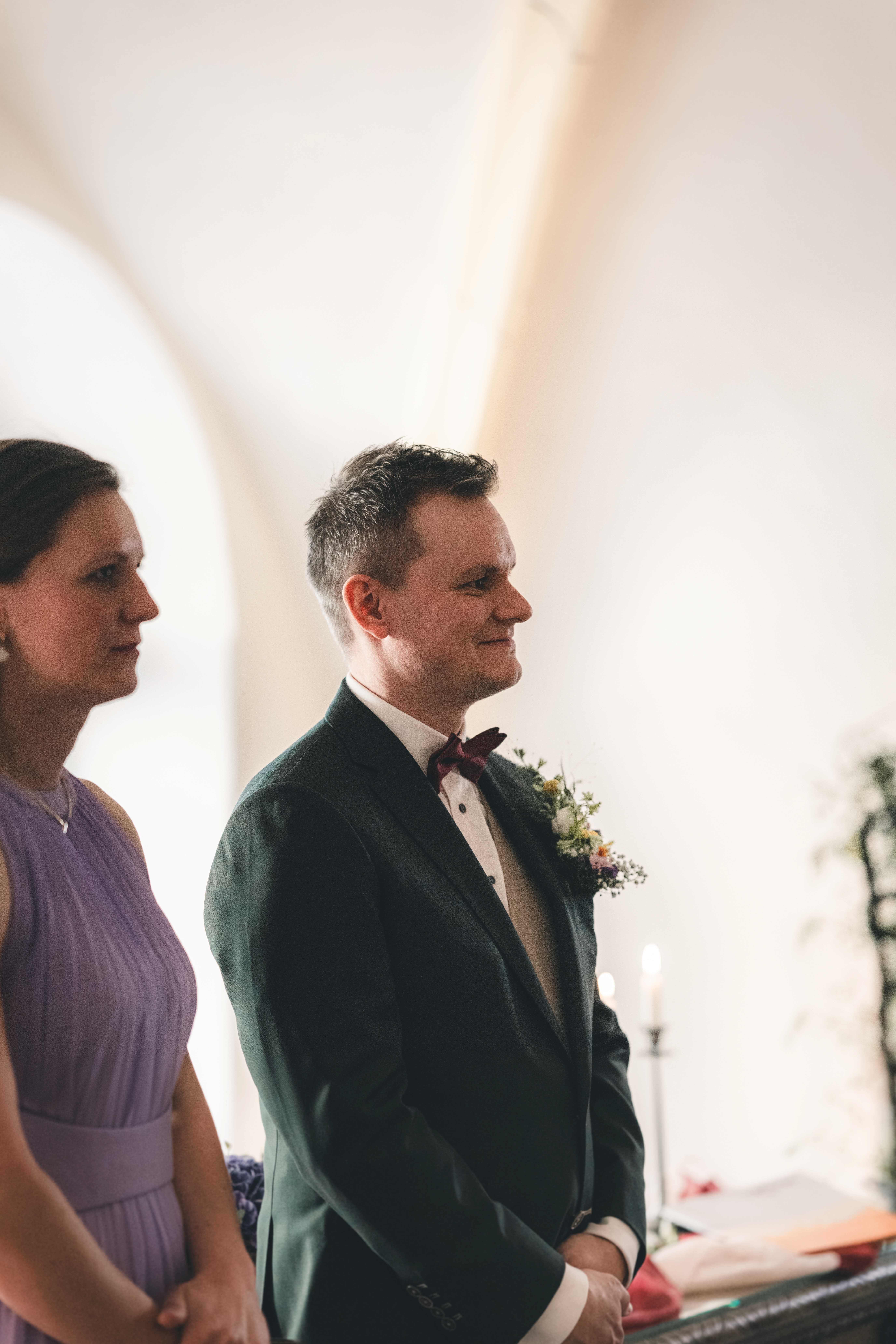 Der Bräutigam im grünen Hochzeitsanzug blickt mit einem glücklichen Lächeln im hellen, gewölbten Trausaal des Rathauses Pirna nach vorn.