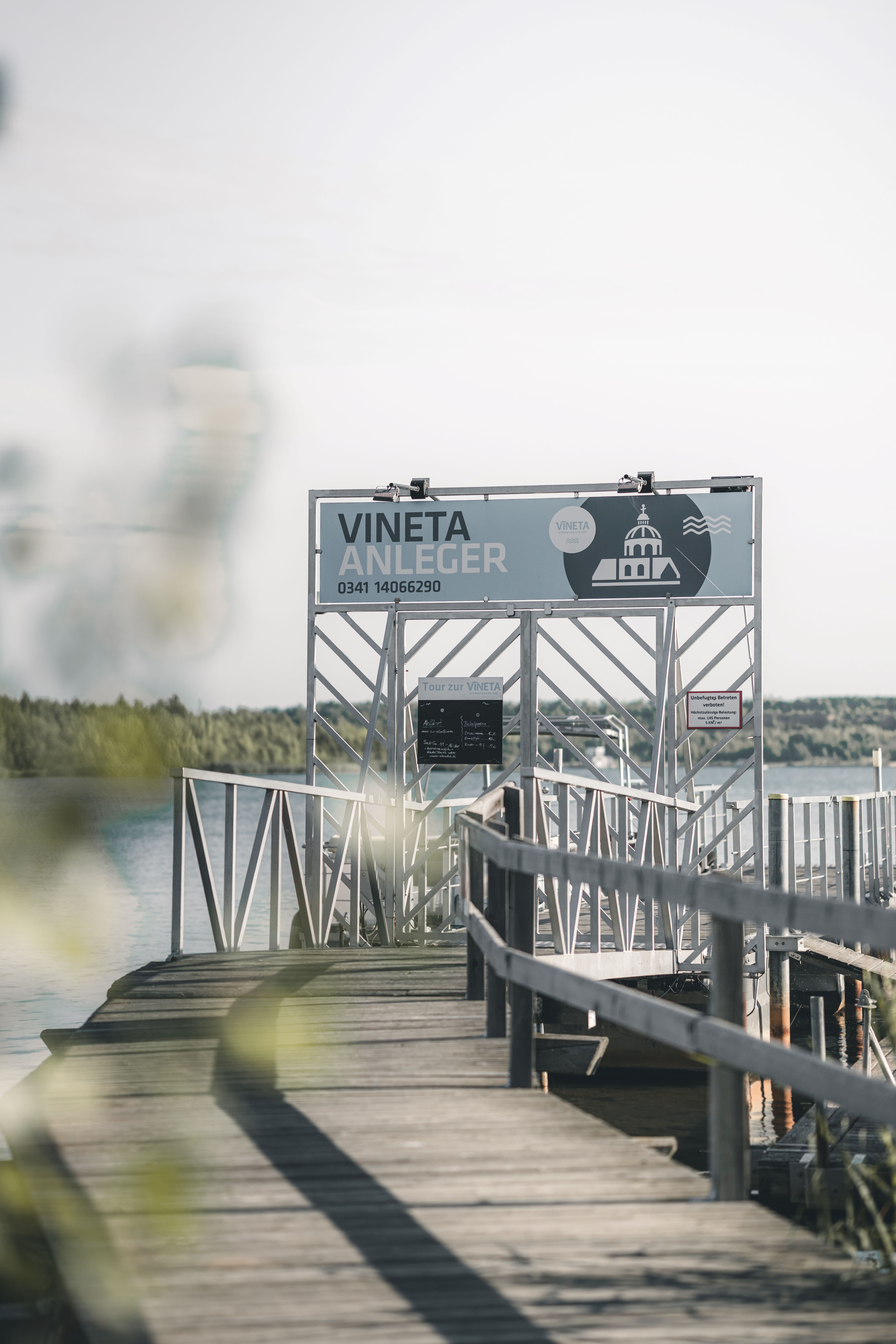 Ein hölzerner Steg führt zum Tor mit der Aufschrift „VINETA ANLEGER“ auf dem Störmthaler See im Leipziger Neuseenland.