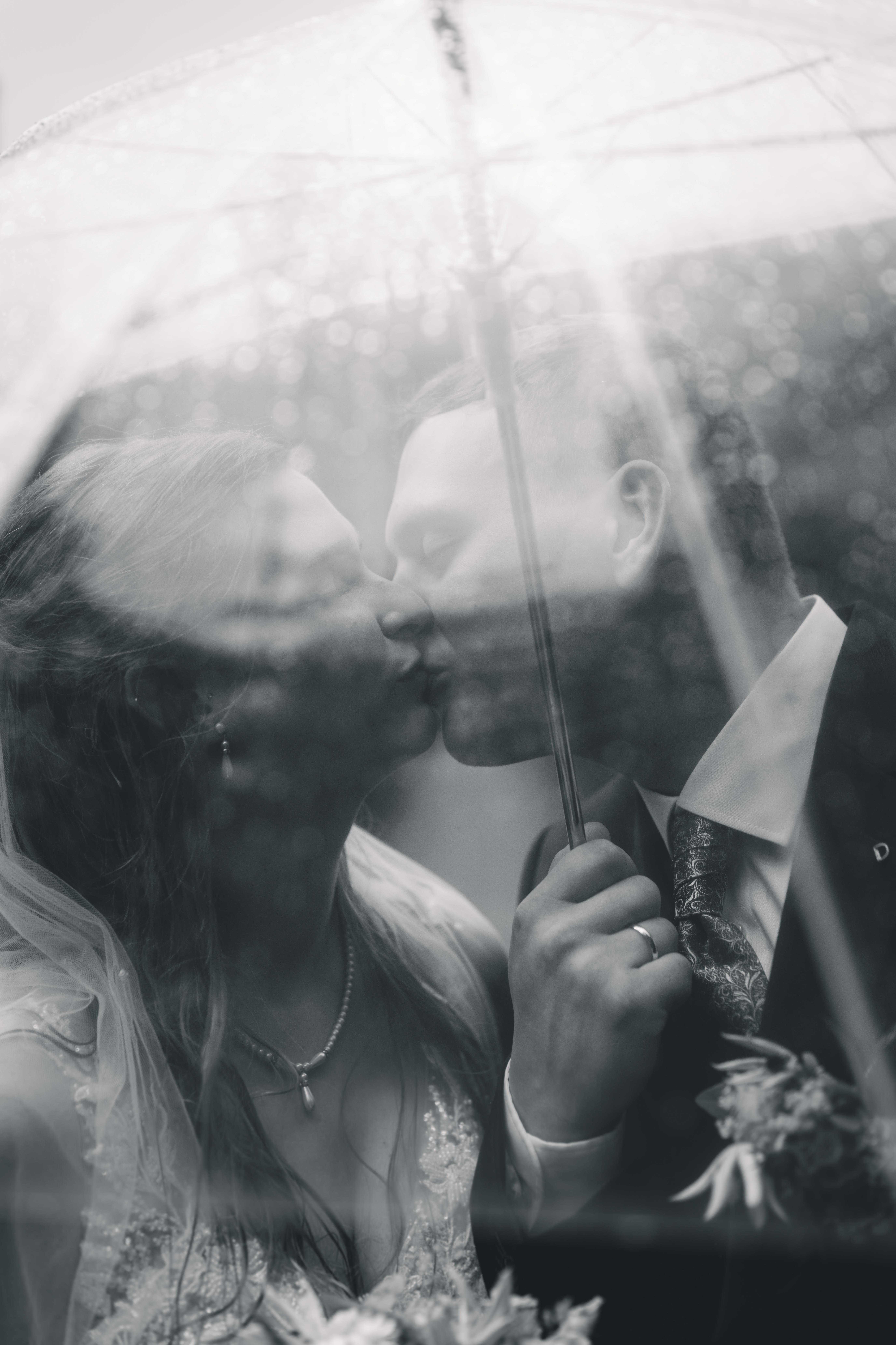 Brautpaar küsst sich unter einem transparenten Regenschirm während eines Brautpaarshootings auf Burg Kriebstein – romantische Hochzeitsreportage